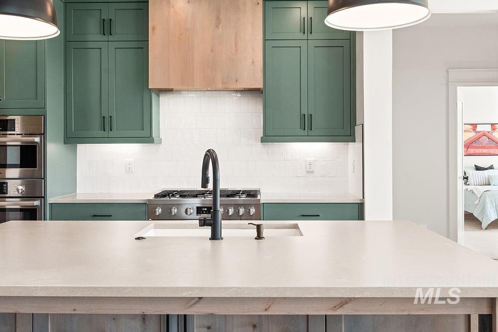 Kitchen with green cabinets, backsplash, and stainless steel double oven