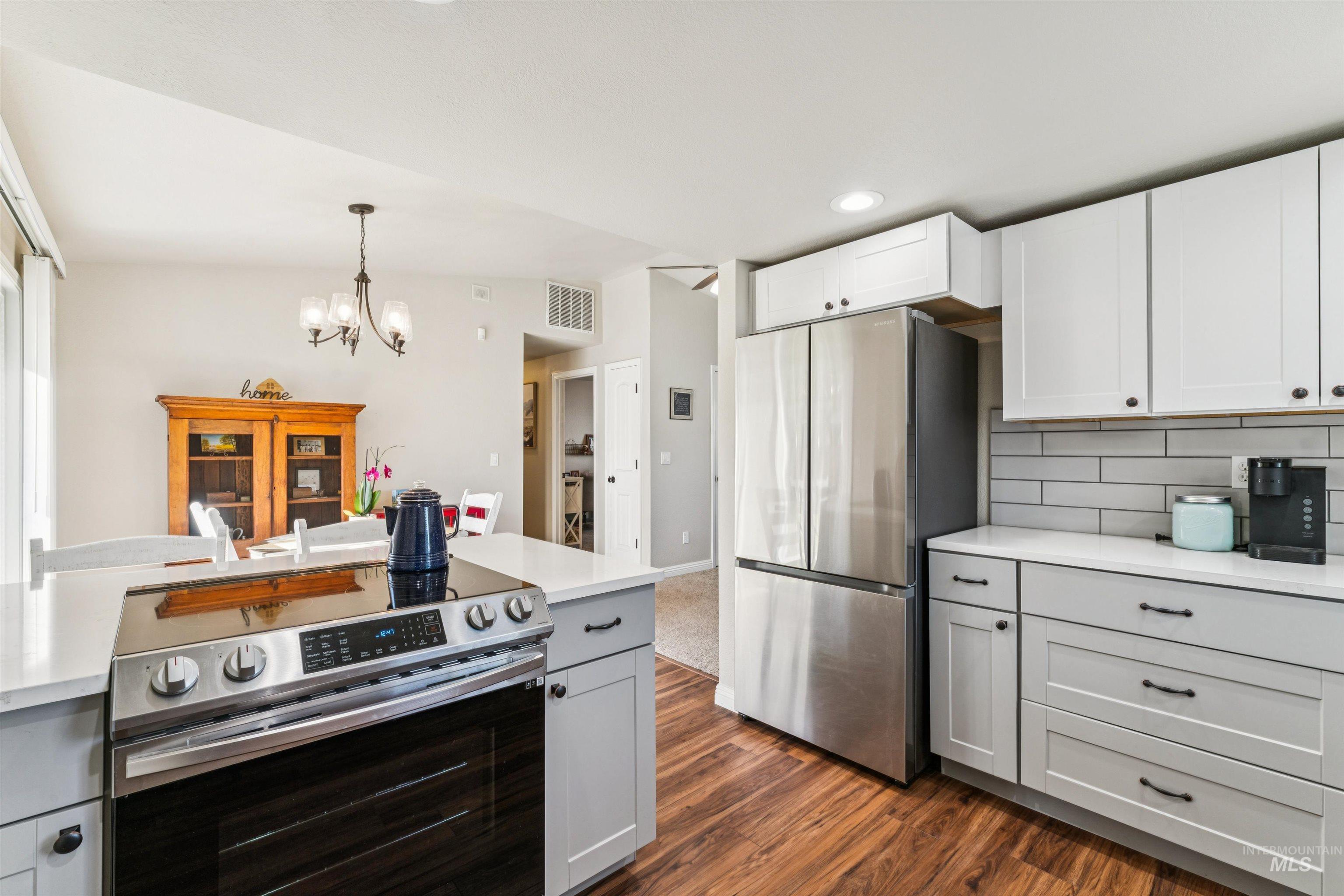 Kitchen featuring stainless steel appliances, white cabinets, decorative light fixtures, gray cabinetry, and tasteful backsplash