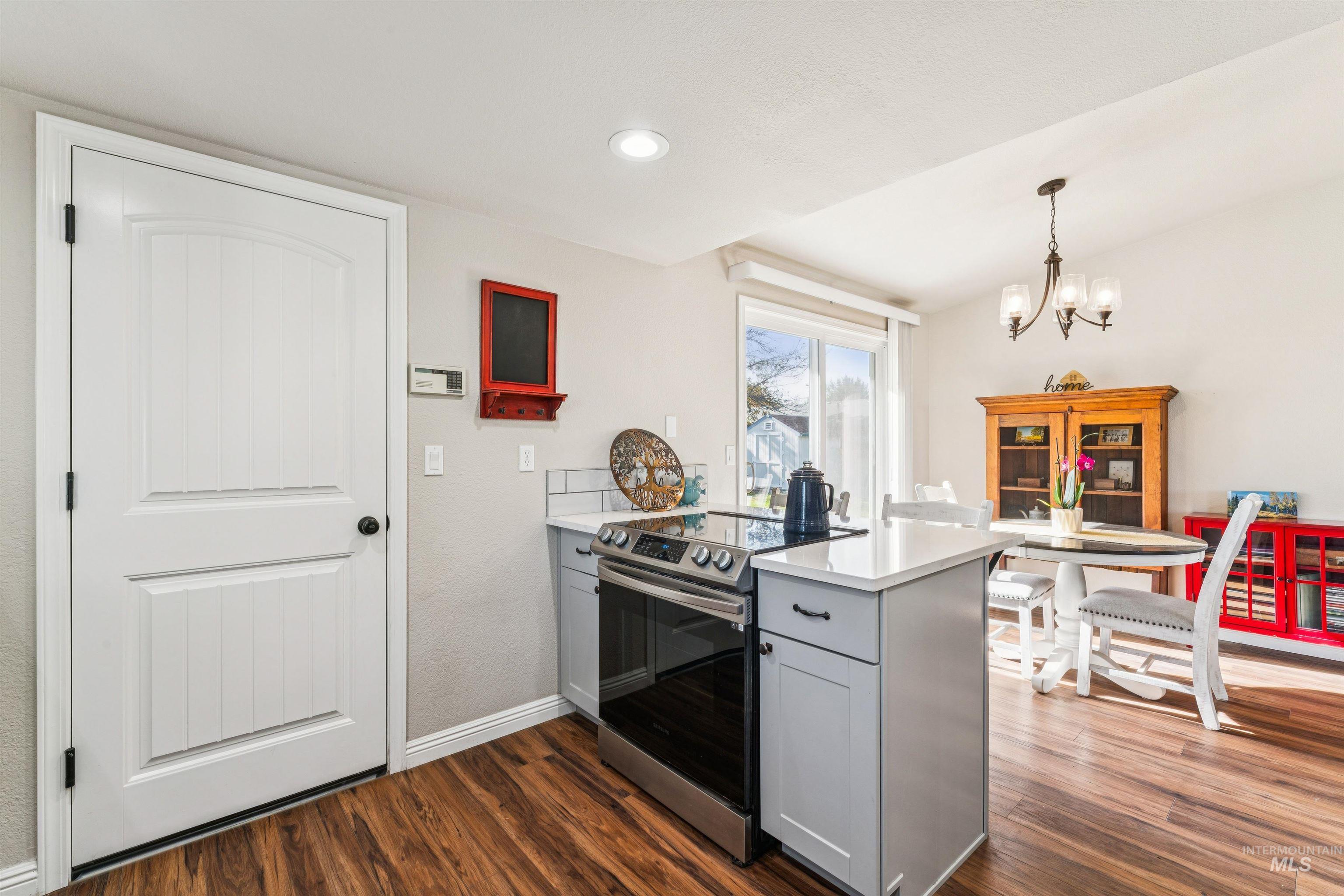 Kitchen featuring a peninsula, stainless steel electric stove, dark wood-style floors, gray cabinets, and a chandelier