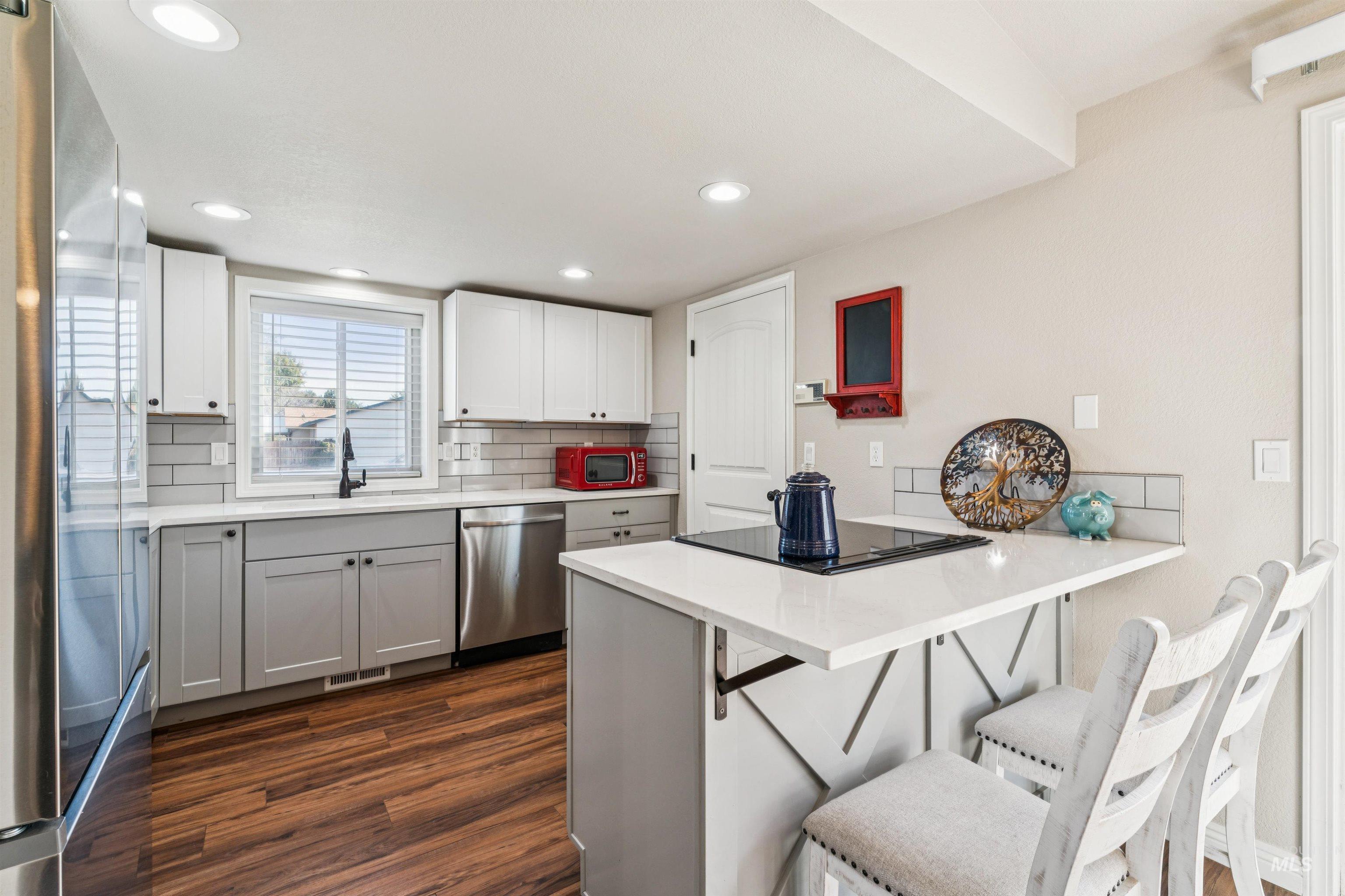Kitchen with a kitchen bar, a peninsula, dark wood-type flooring, appliances with stainless steel finishes, and white cabinets