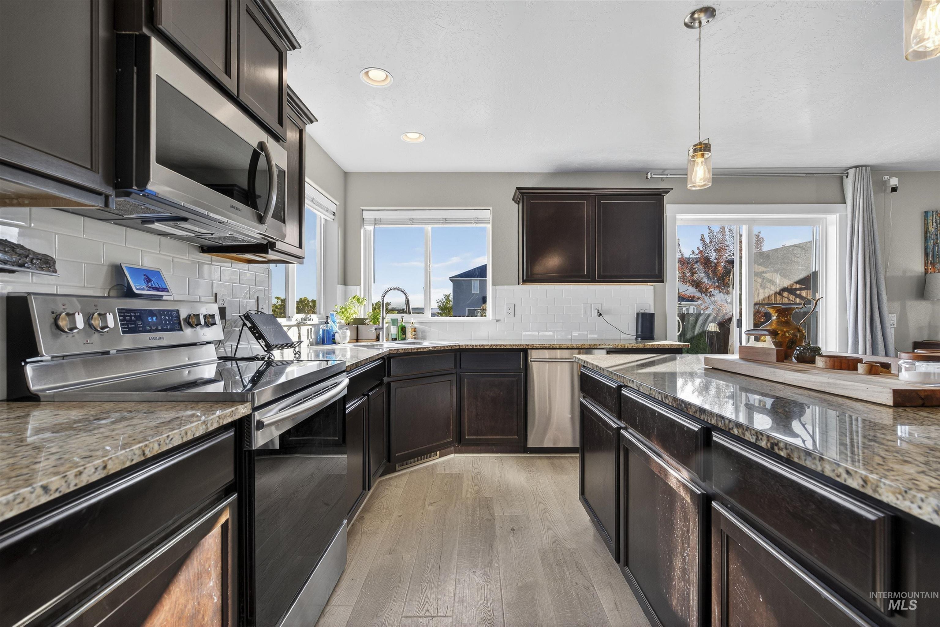 Kitchen featuring stainless steel appliances, dark stone counters, decorative backsplash, dark brown cabinets, and light wood-style floors