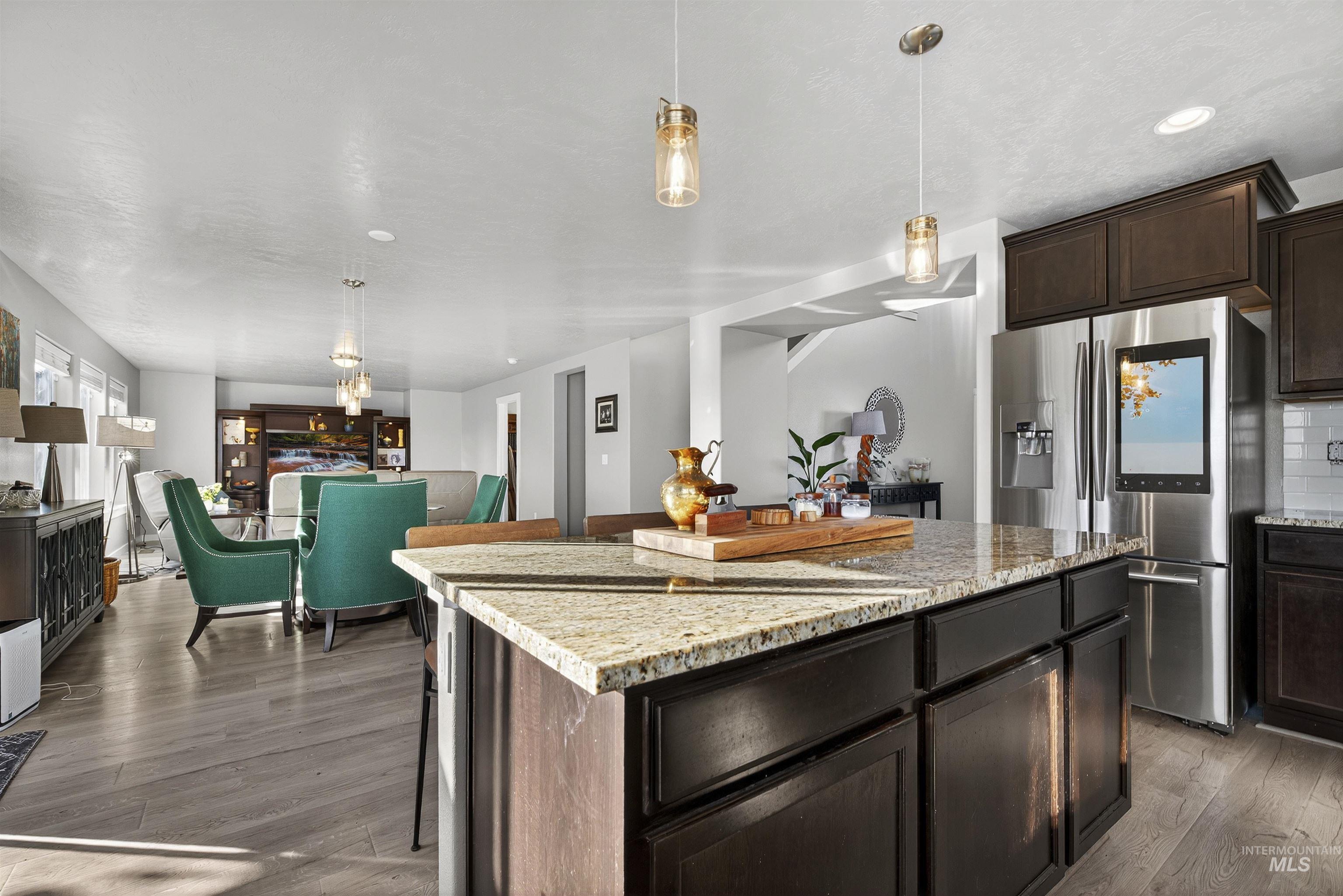 Kitchen featuring dark brown cabinetry, decorative light fixtures, light stone countertops, stainless steel fridge, and dark wood-style floors