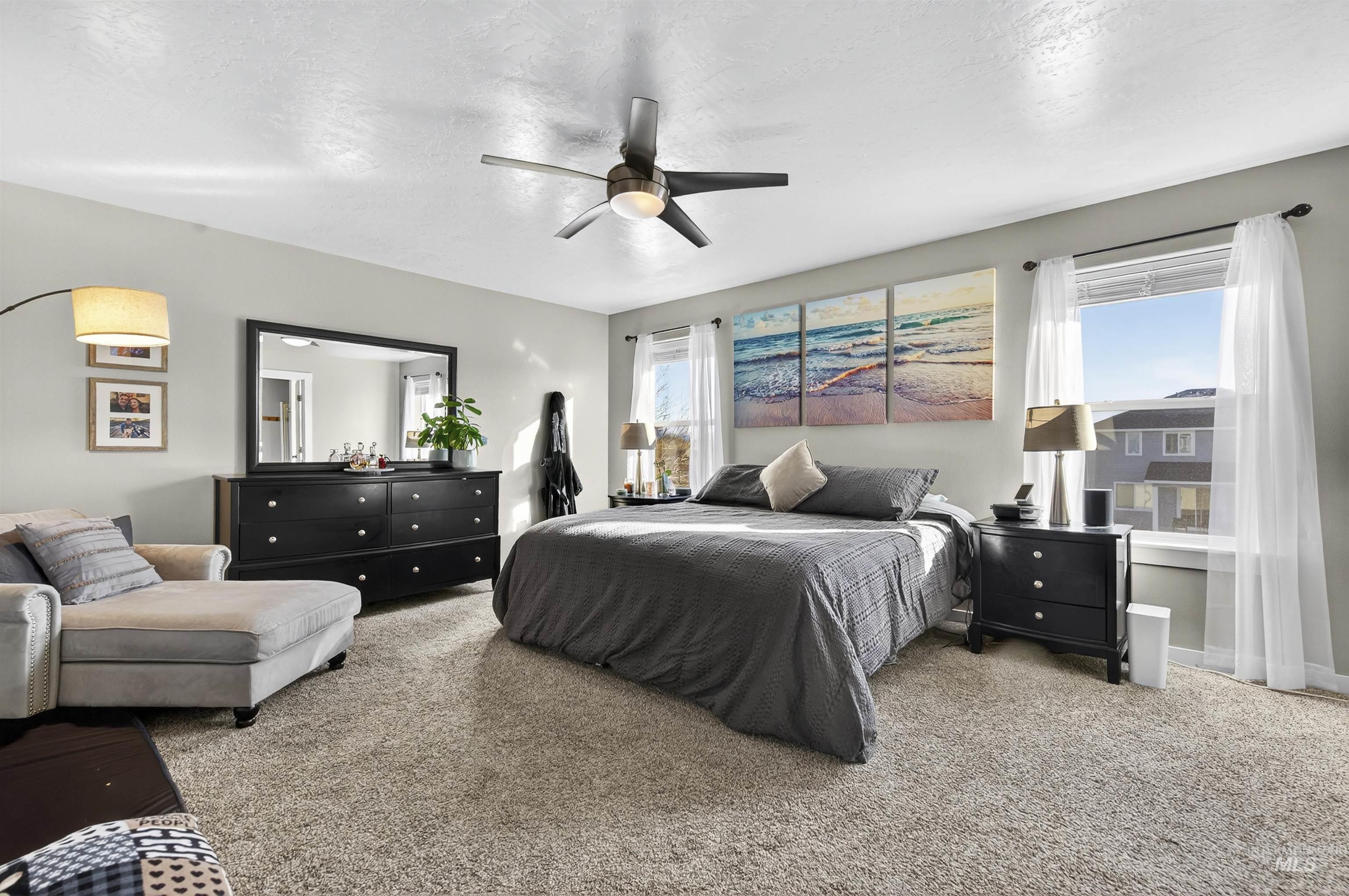 Bedroom featuring light carpet, multiple windows, a textured ceiling, and ceiling fan
