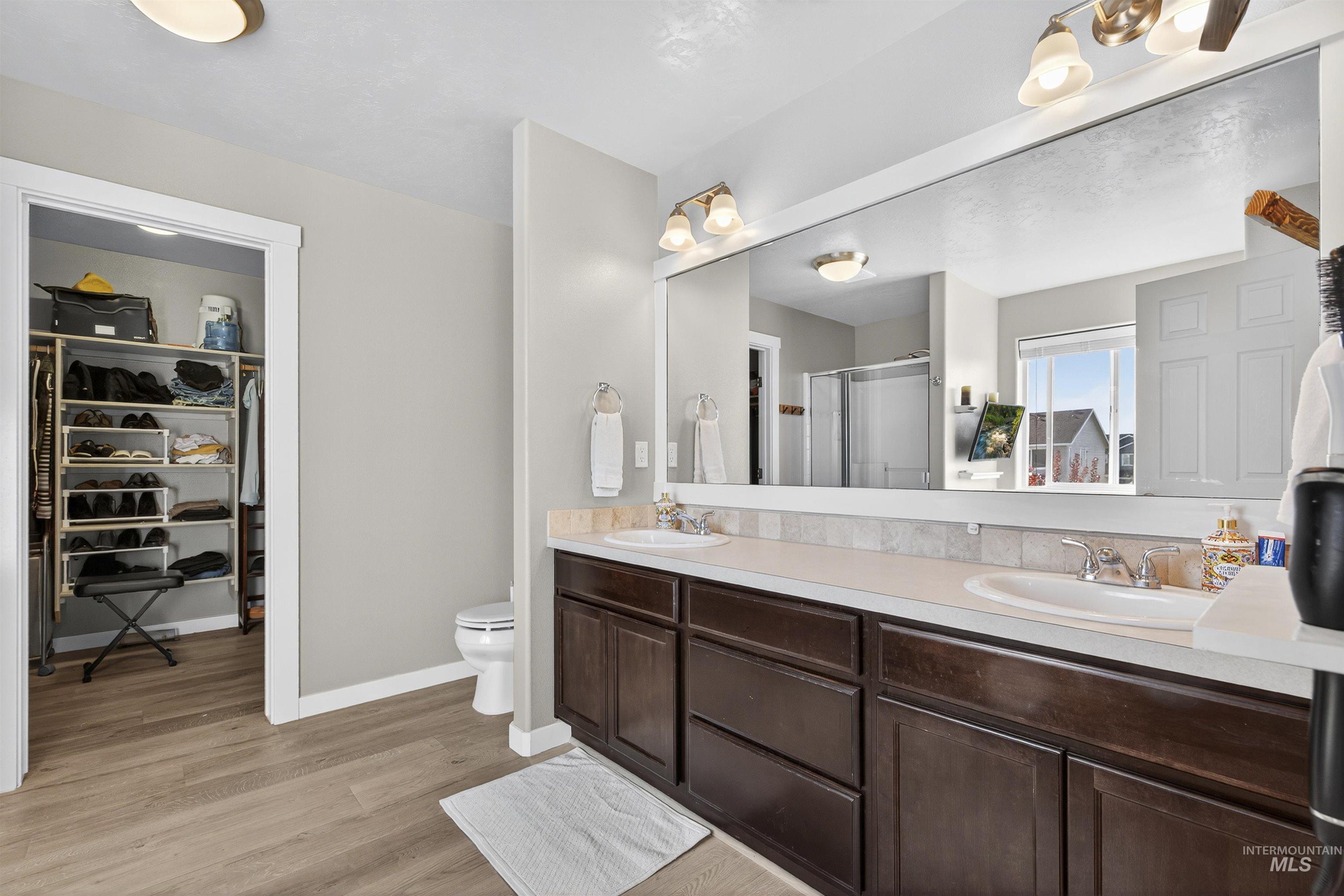Full bath with a walk in closet, a stall shower, double vanity, and light wood-style floors