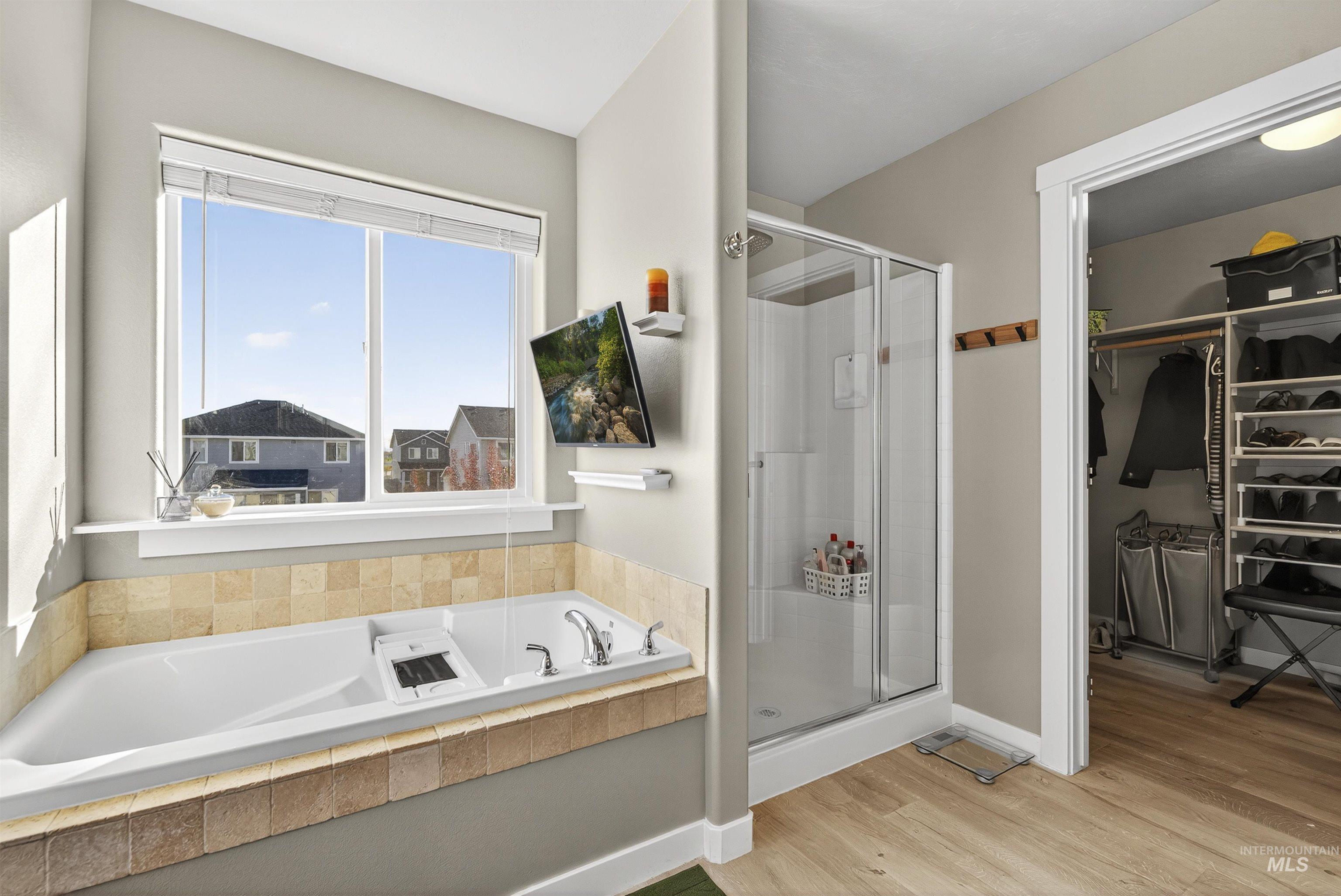 Bathroom featuring a stall shower, a spacious closet, light wood finished floors, and a garden tub