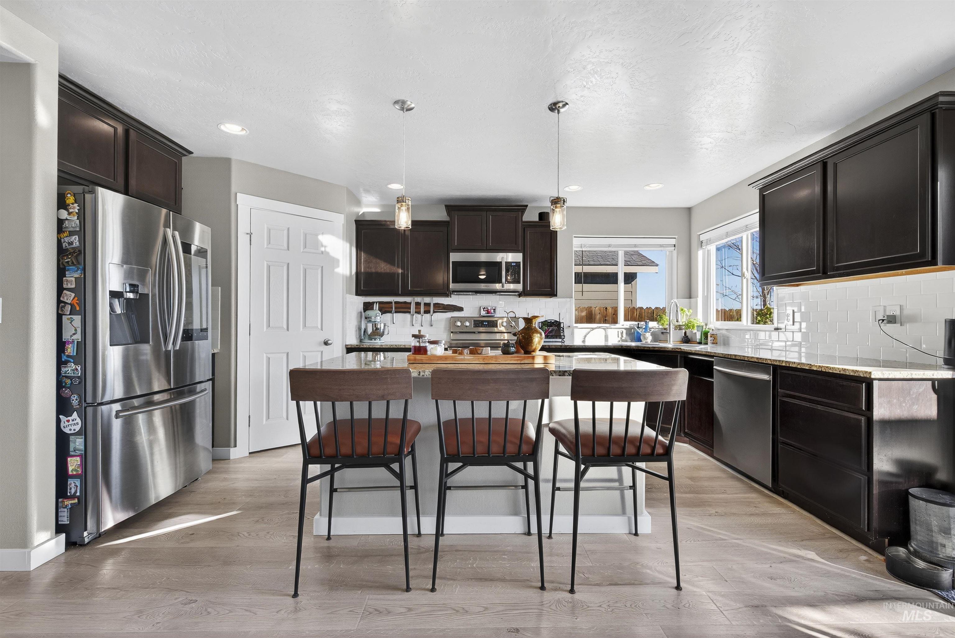 Kitchen with appliances with stainless steel finishes, decorative light fixtures, light wood-type flooring, decorative backsplash, and dark brown cabinets