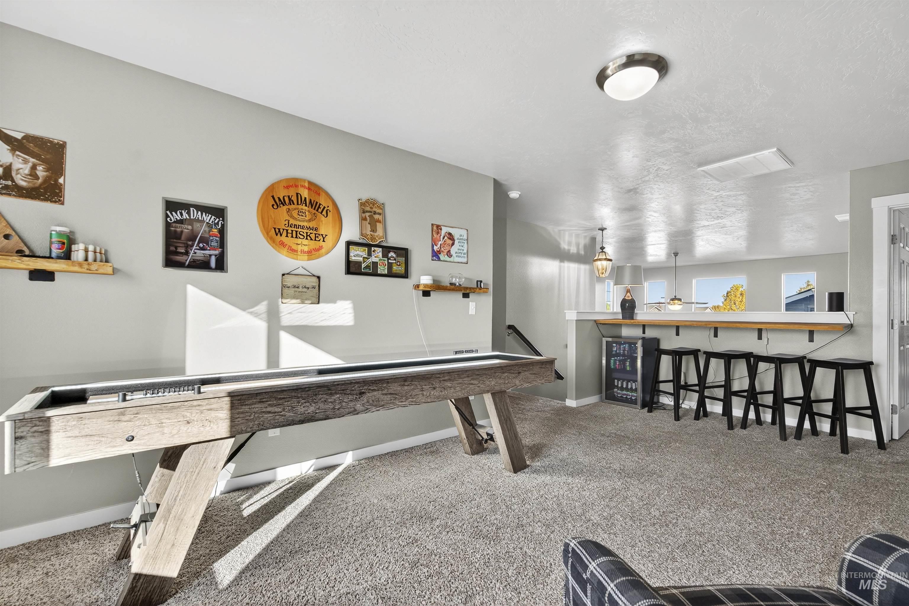 Rec room with light carpet, a textured ceiling, and a dry bar