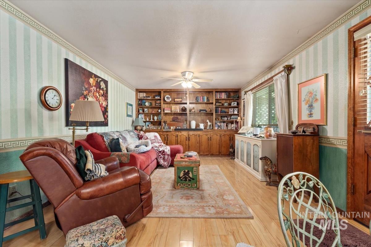 Living room featuring wallpapered walls, crown molding, light wood finished floors, and a ceiling fan