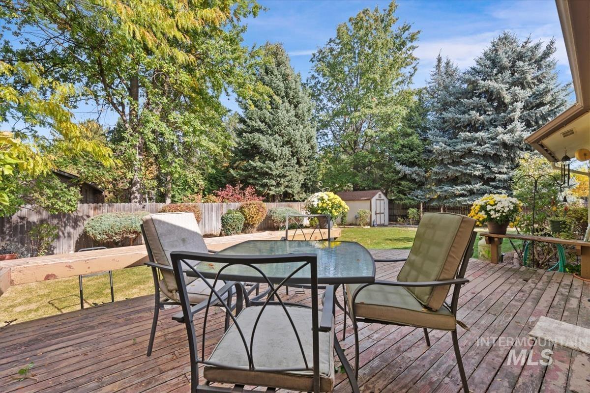 Wooden deck featuring outdoor dining area, a shed, view of wooded area, and a fenced backyard