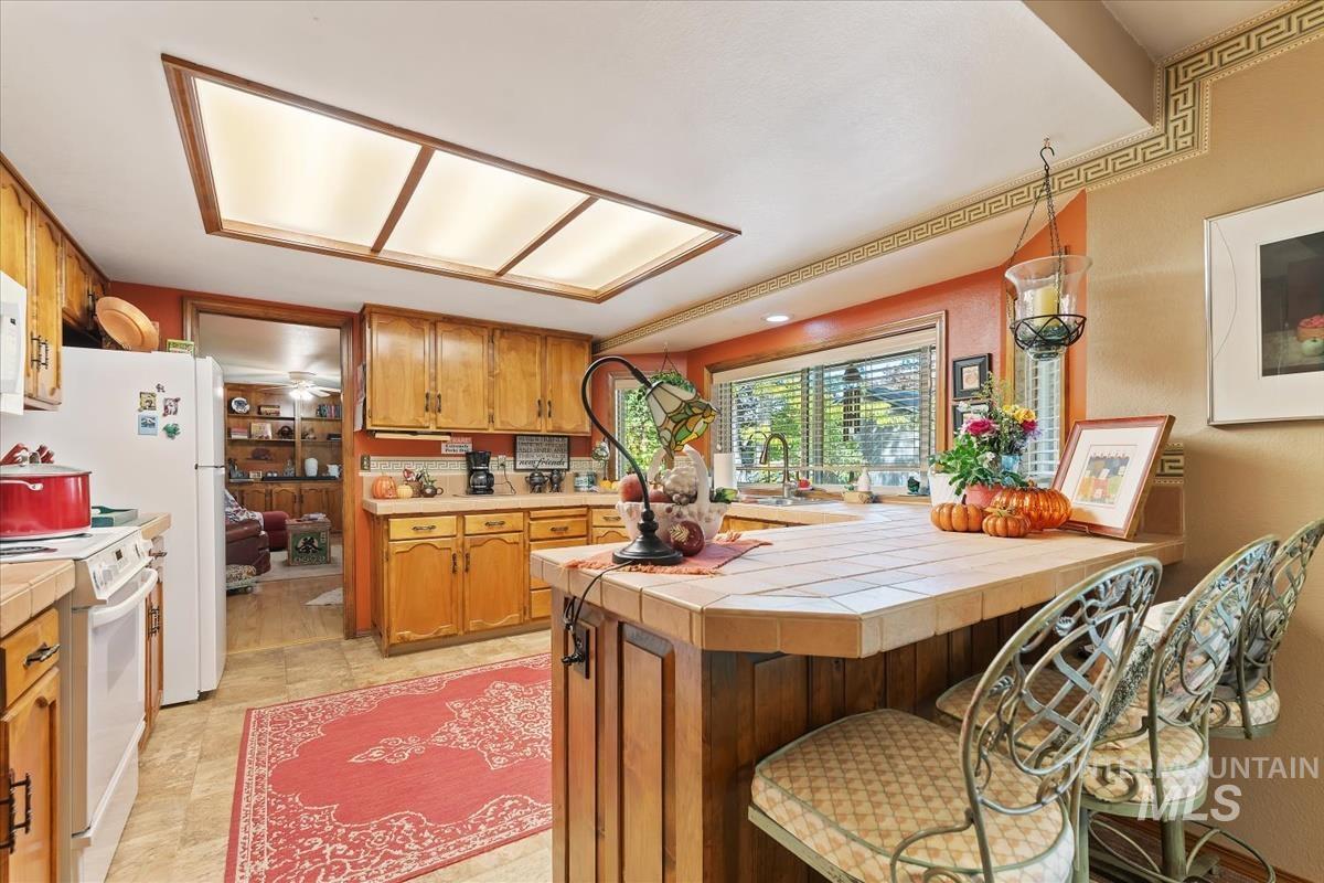 Kitchen featuring tile counters, a peninsula, brown cabinetry, and white appliances