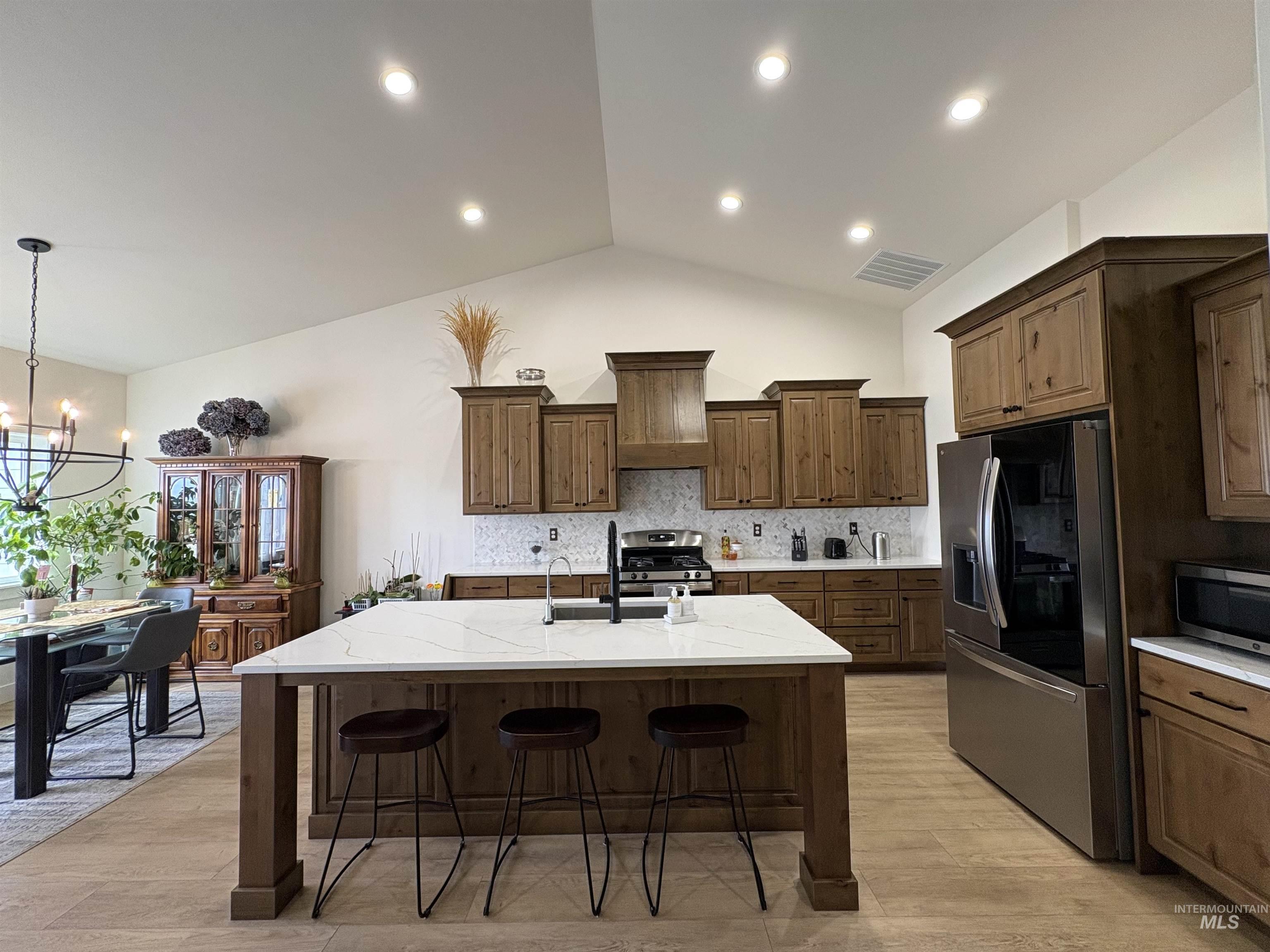 Kitchen with backsplash, stainless steel appliances, a breakfast bar area, vaulted ceiling, and a center island with sink