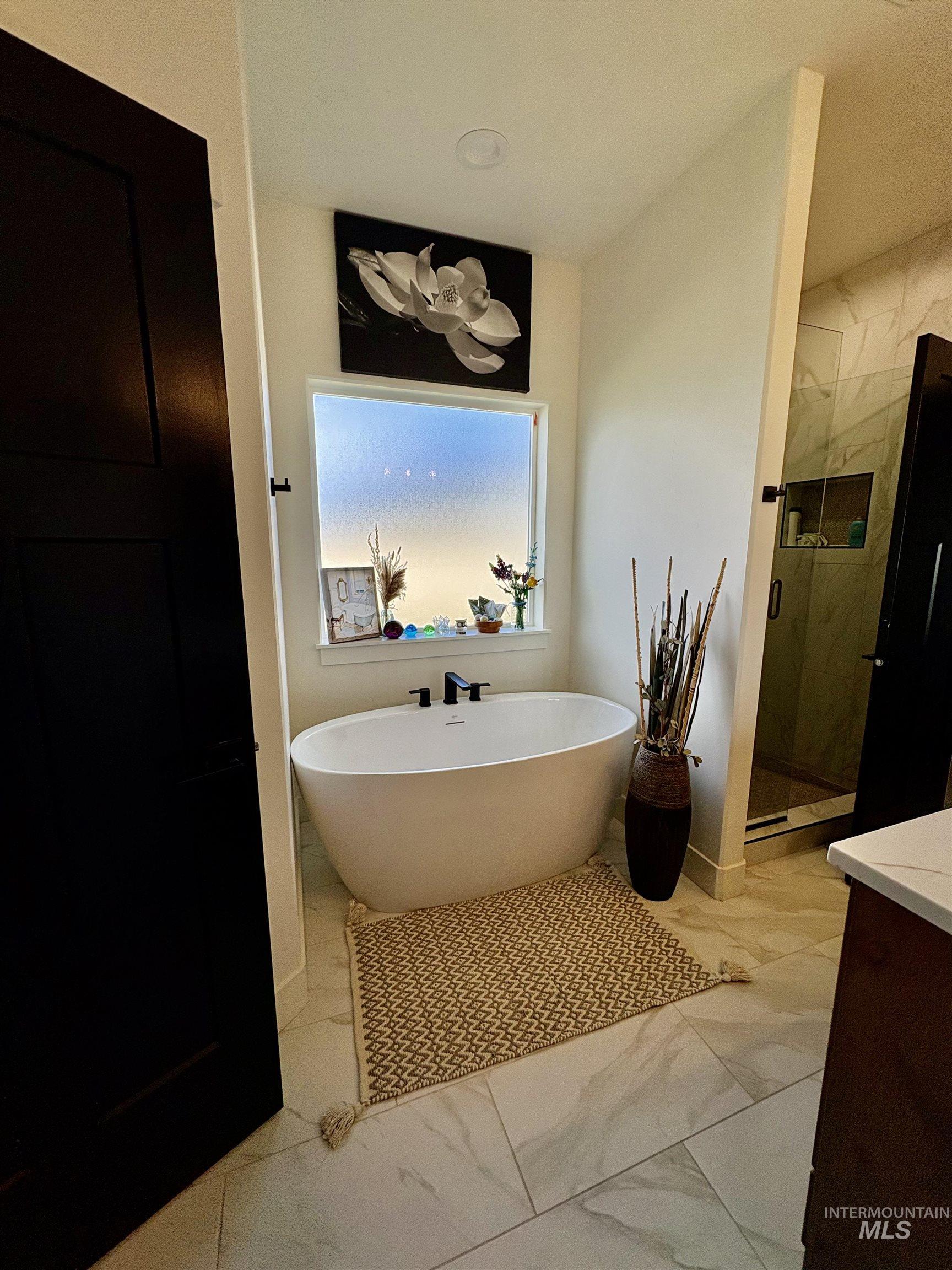 Bathroom with light marble finish flooring, a freestanding tub, a marble finish shower, and vanity