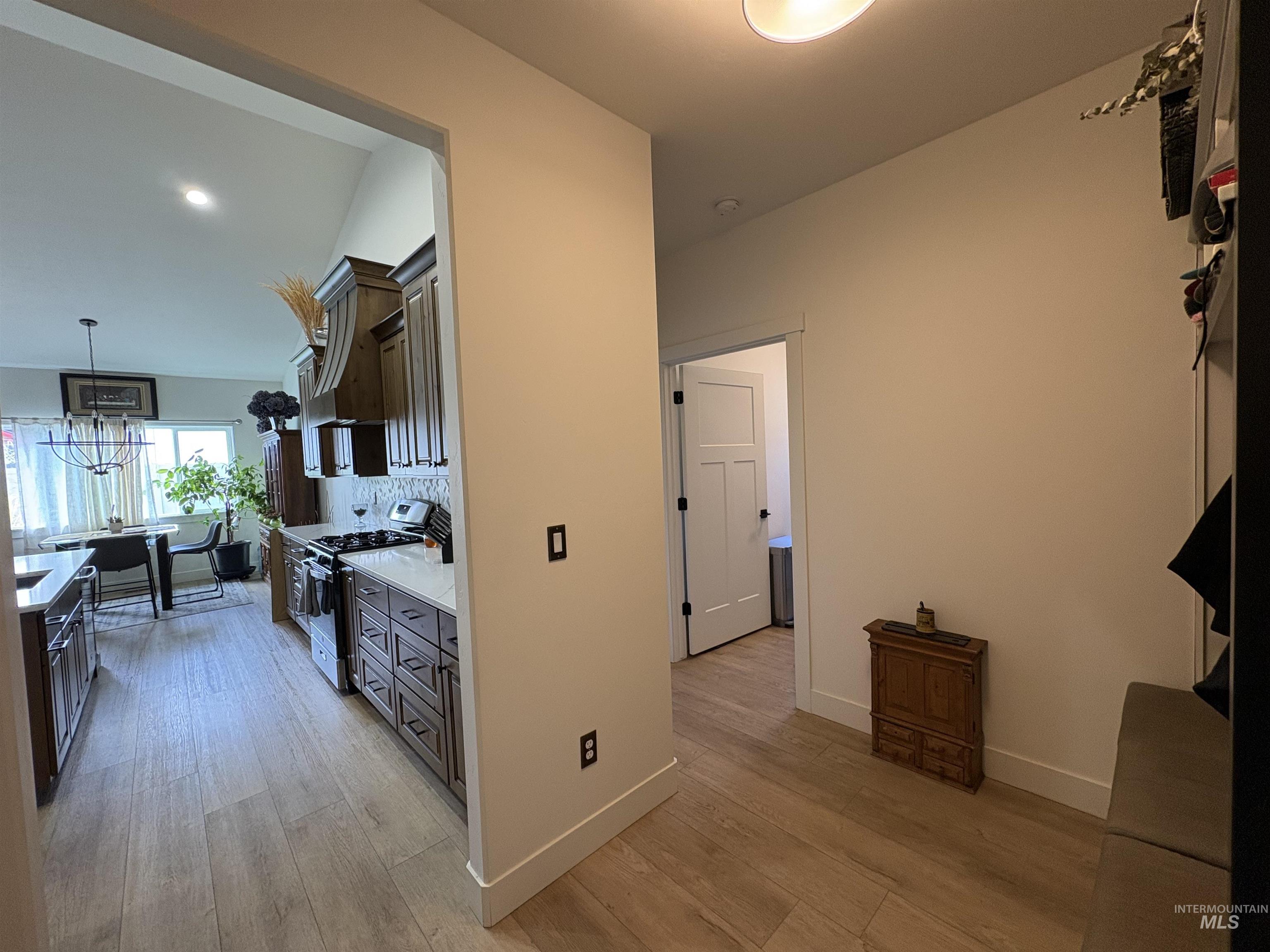 Kitchen with tasteful backsplash, stainless steel range with gas cooktop, pendant lighting, custom range hood, and light wood finished floors