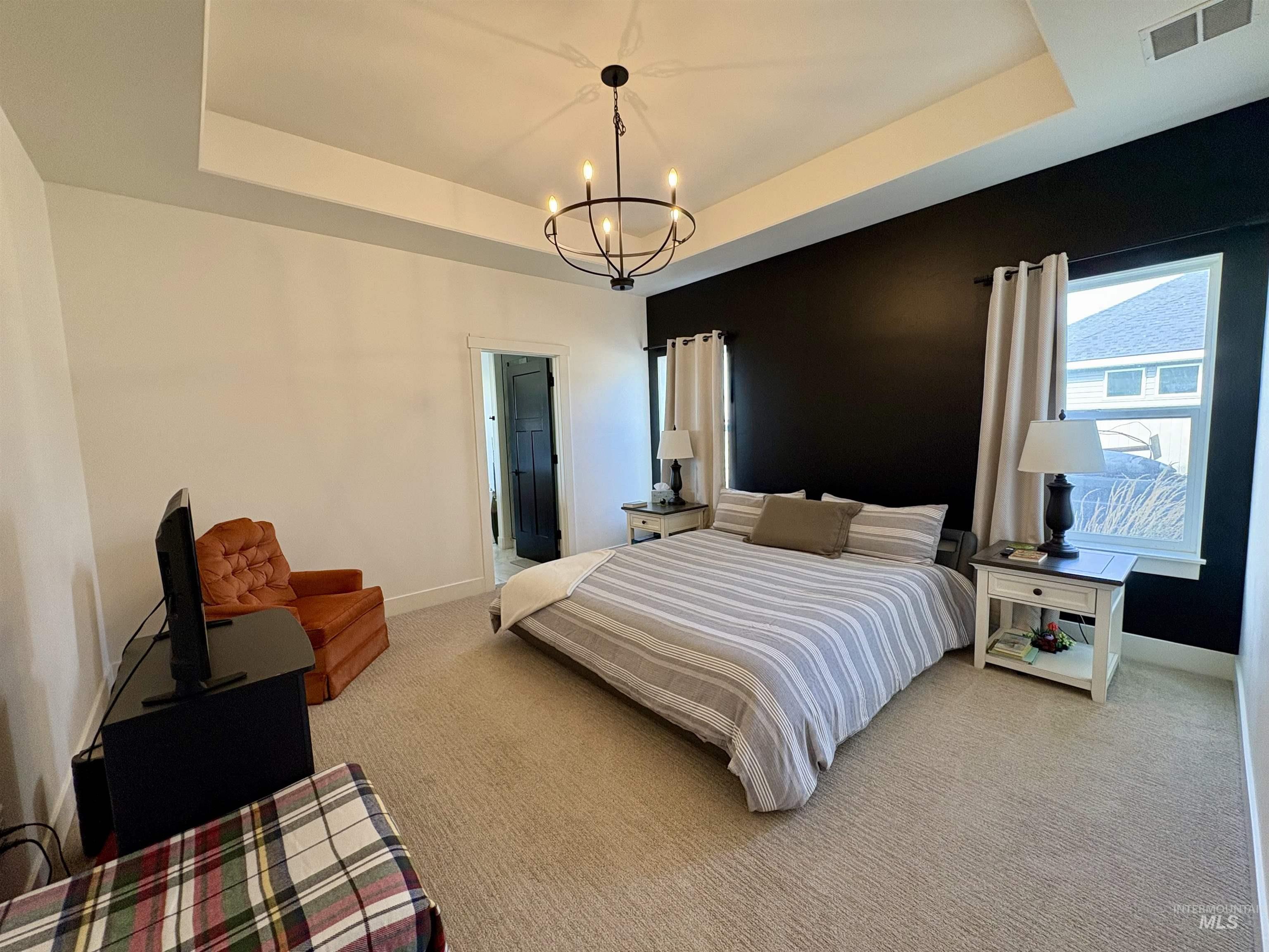 Carpeted bedroom featuring a tray ceiling and a chandelier