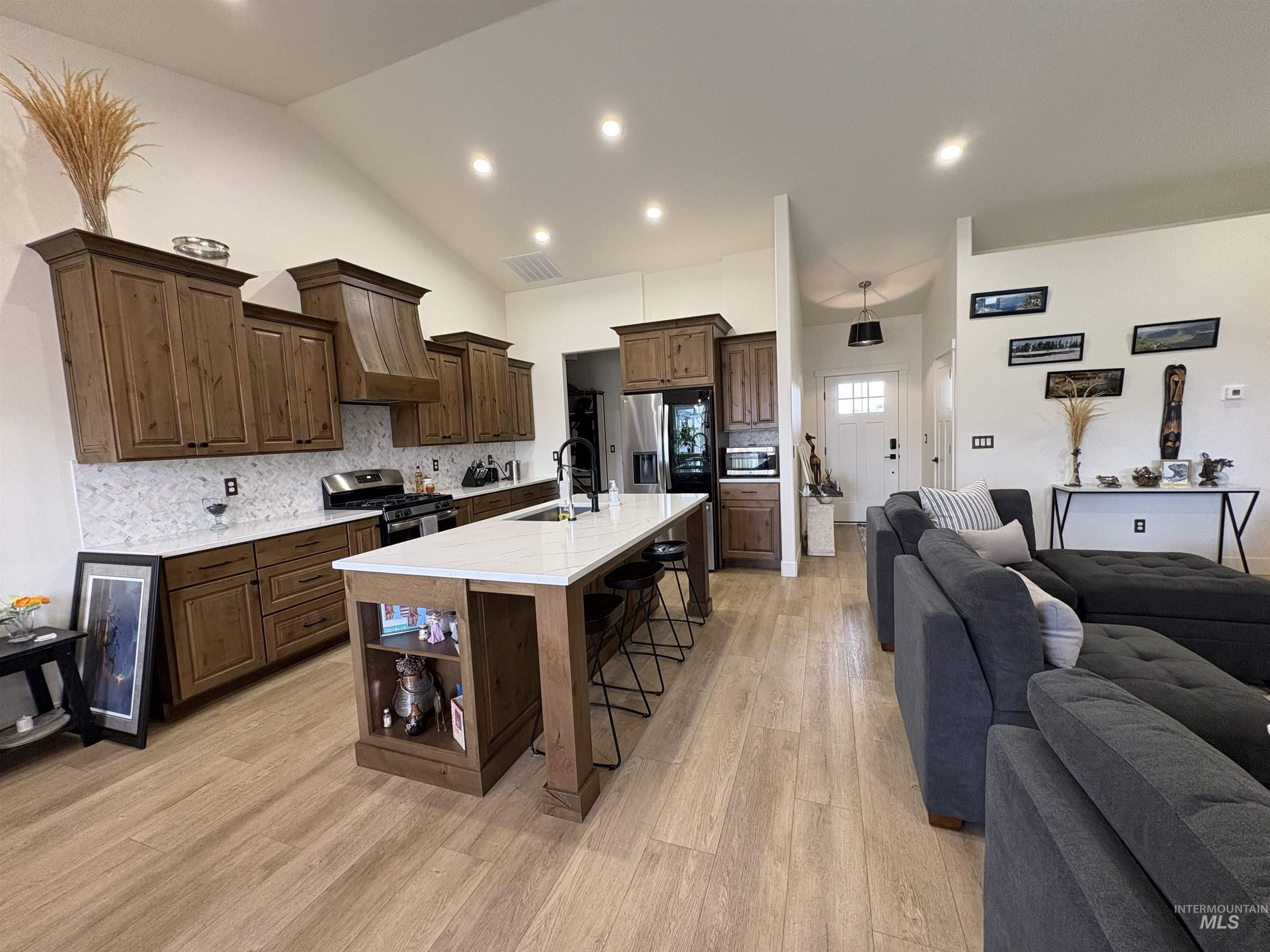 Kitchen with a breakfast bar, decorative backsplash, a kitchen island with sink, recessed lighting, and light wood-type flooring