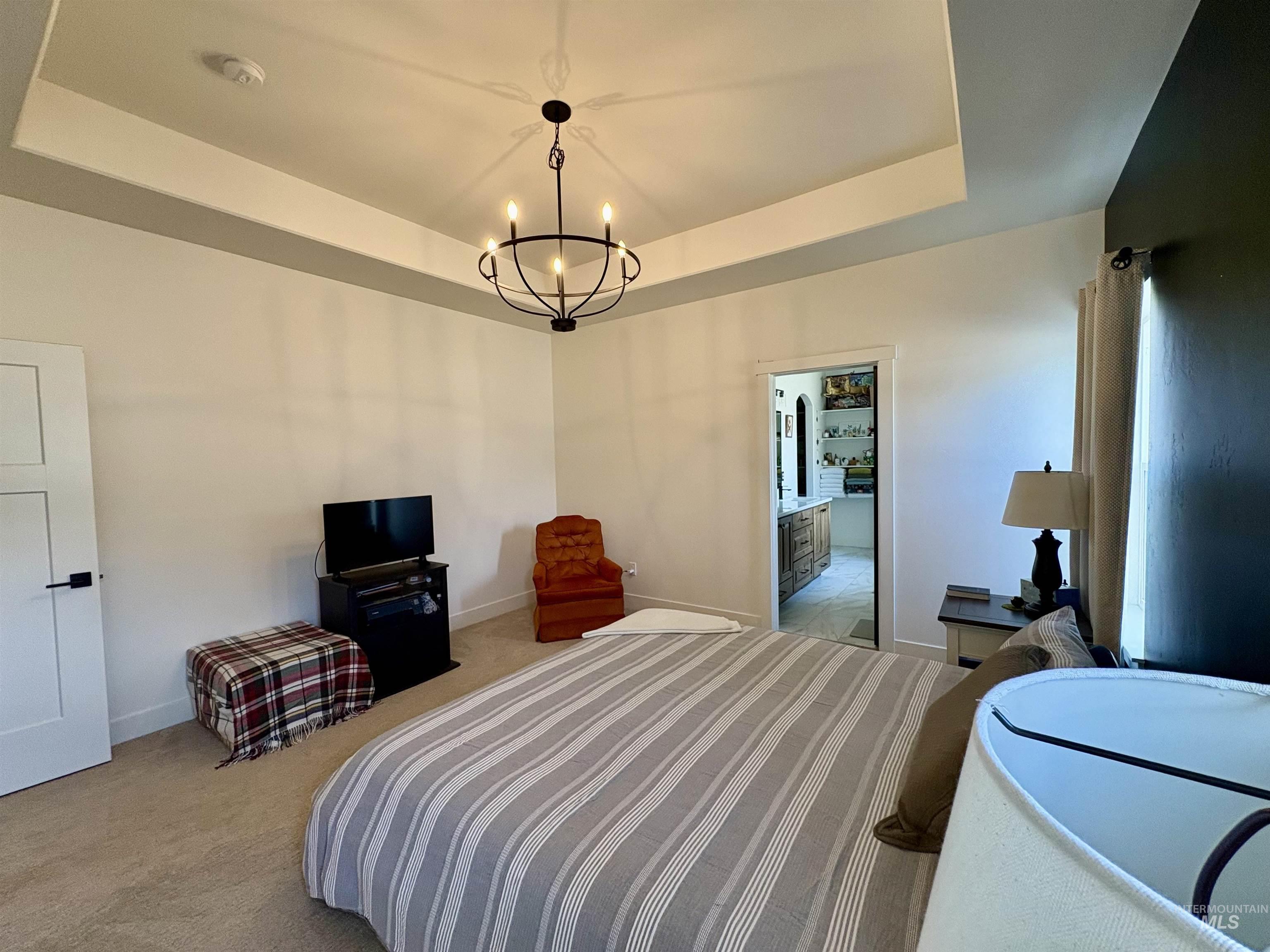 Bedroom featuring a tray ceiling, a chandelier, and light carpet