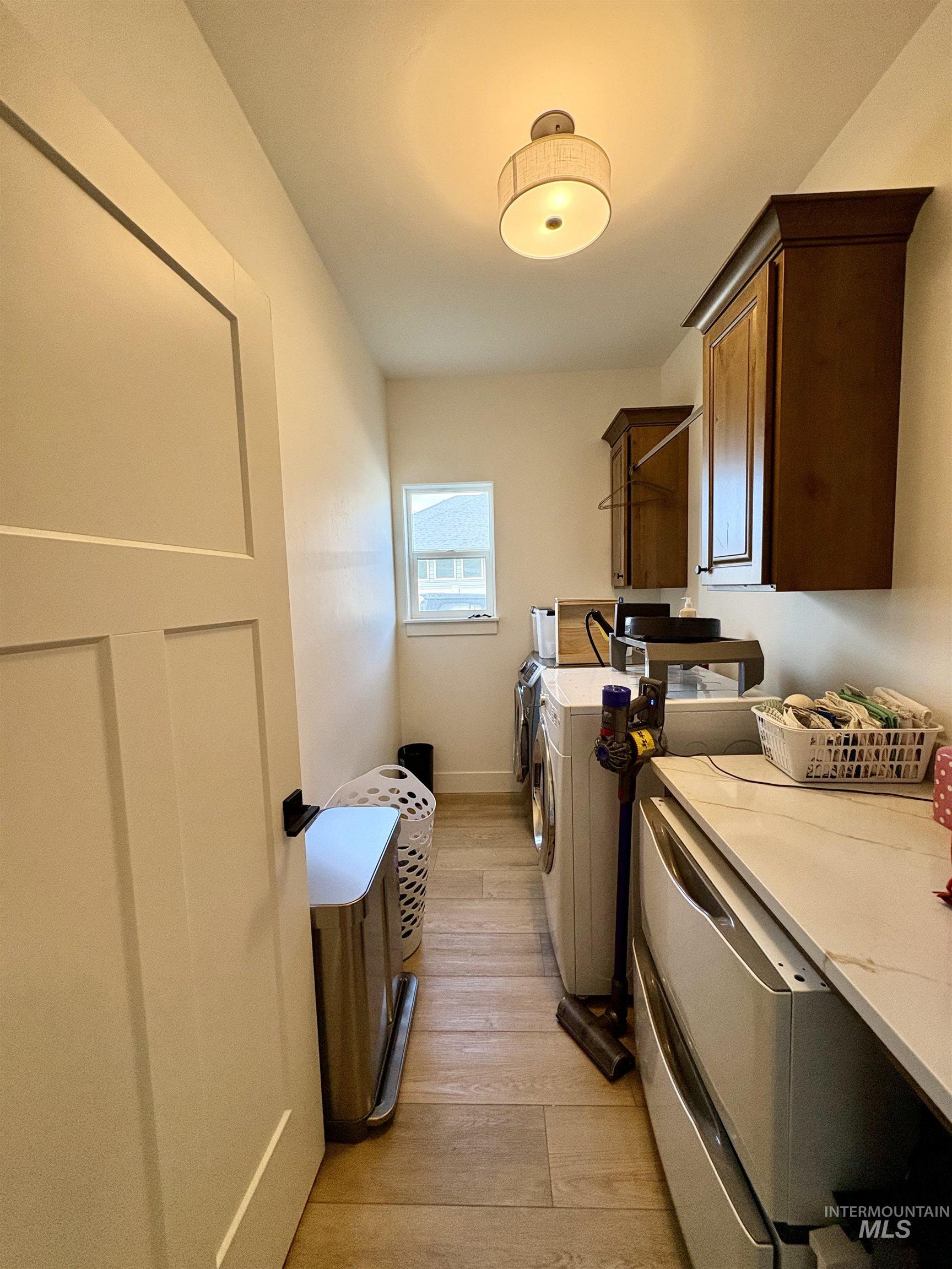 Washroom with cabinet space, light wood finished floors, and washing machine and clothes dryer