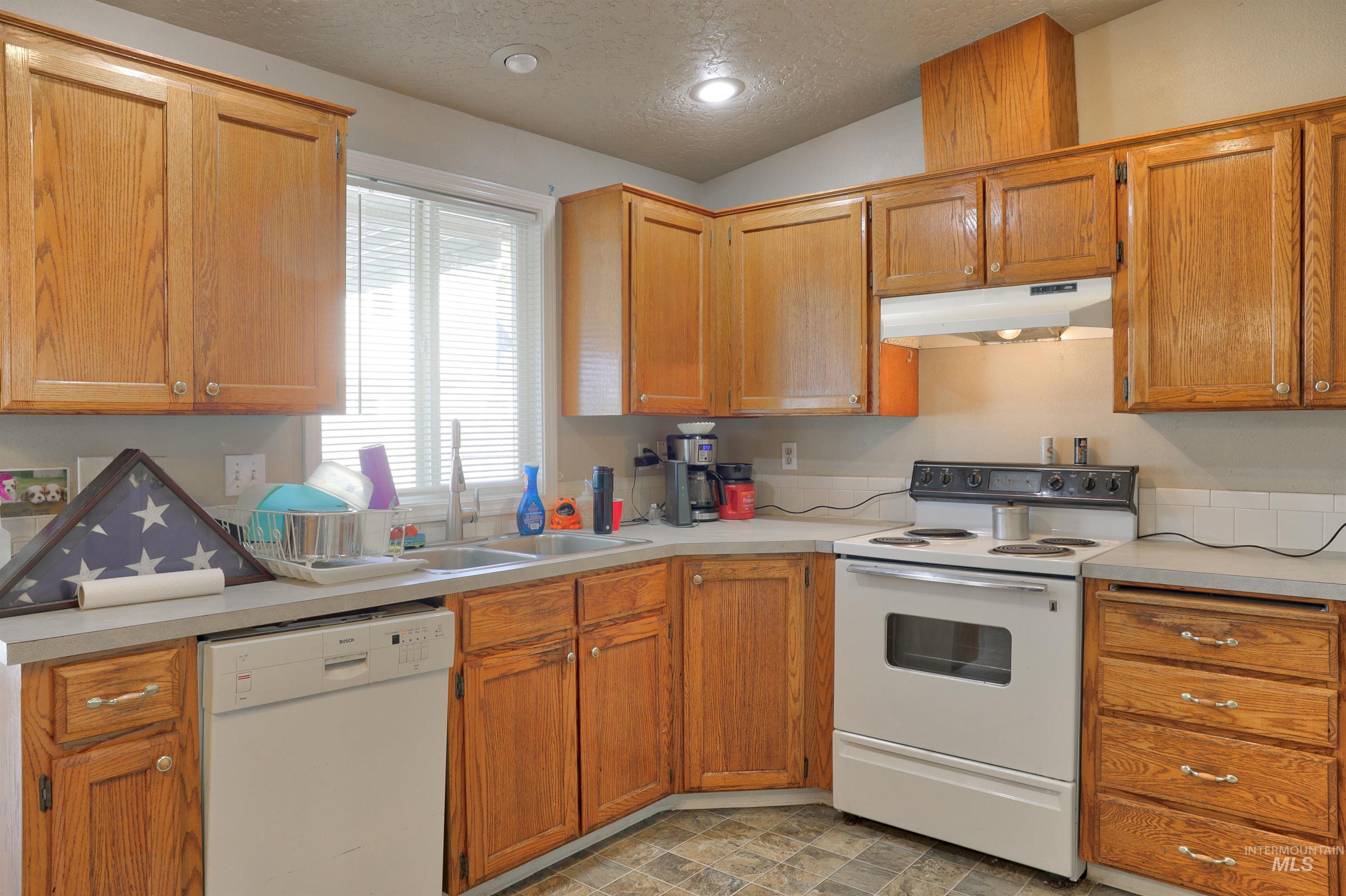 Kitchen with white appliances, a textured ceiling, light countertops, under cabinet range hood, and lofted ceiling