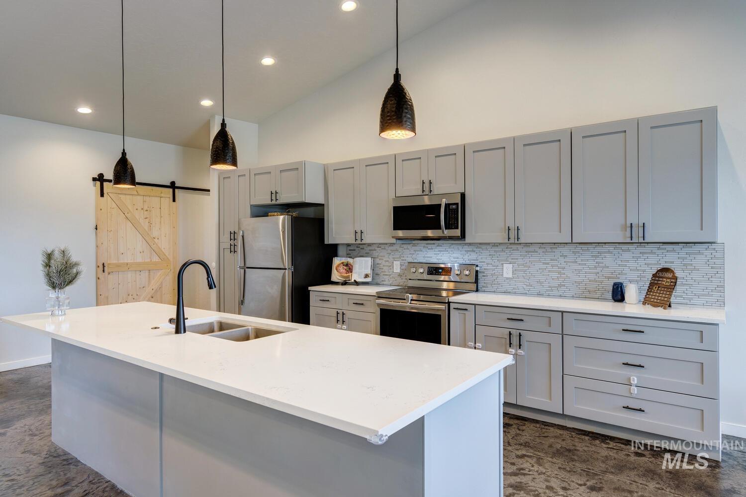 Kitchen featuring gray cabinets, a barn door, pendant lighting, stainless steel appliances, and tasteful backsplash