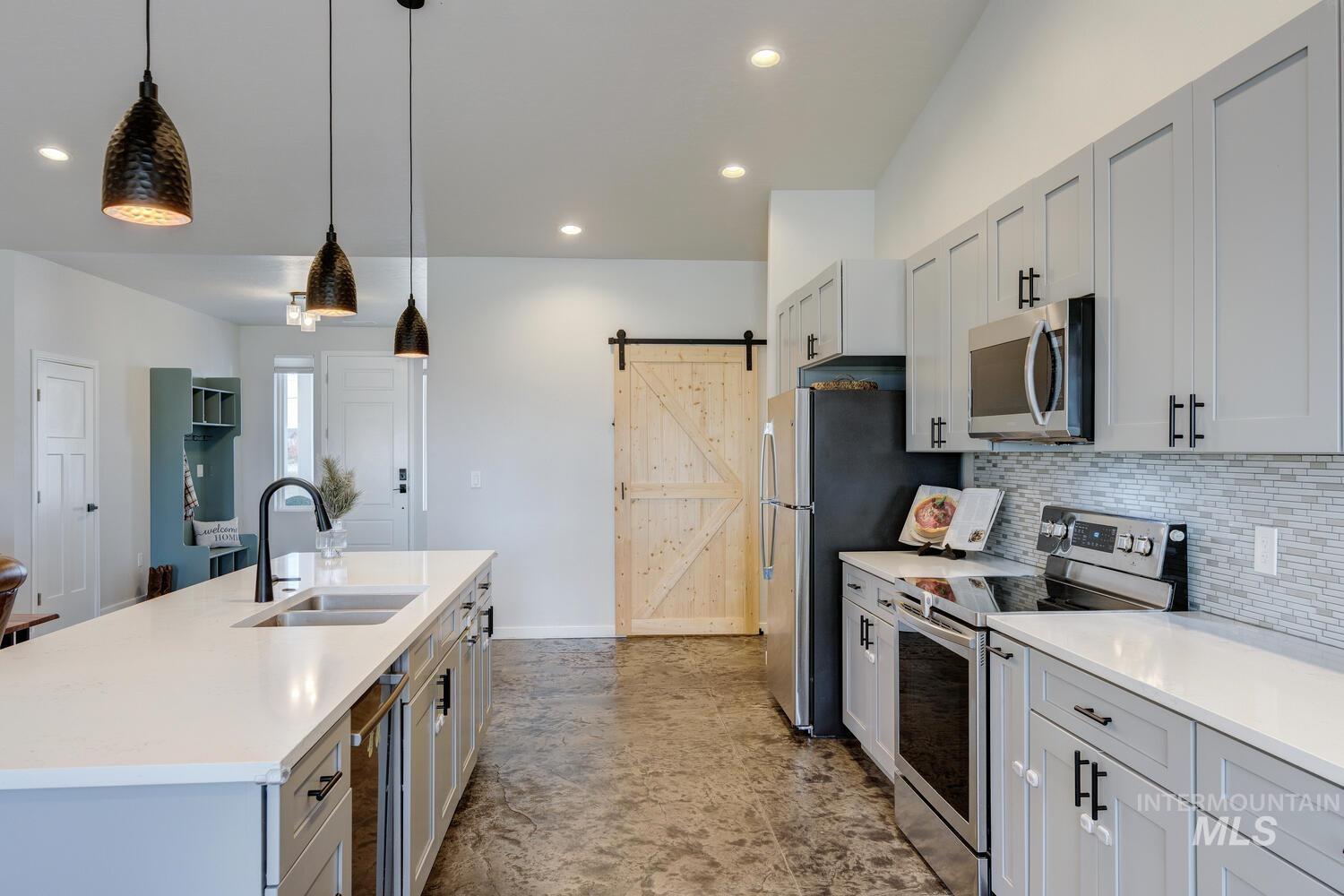 Kitchen featuring appliances with stainless steel finishes, pendant lighting, gray cabinetry, a barn door, and recessed lighting
