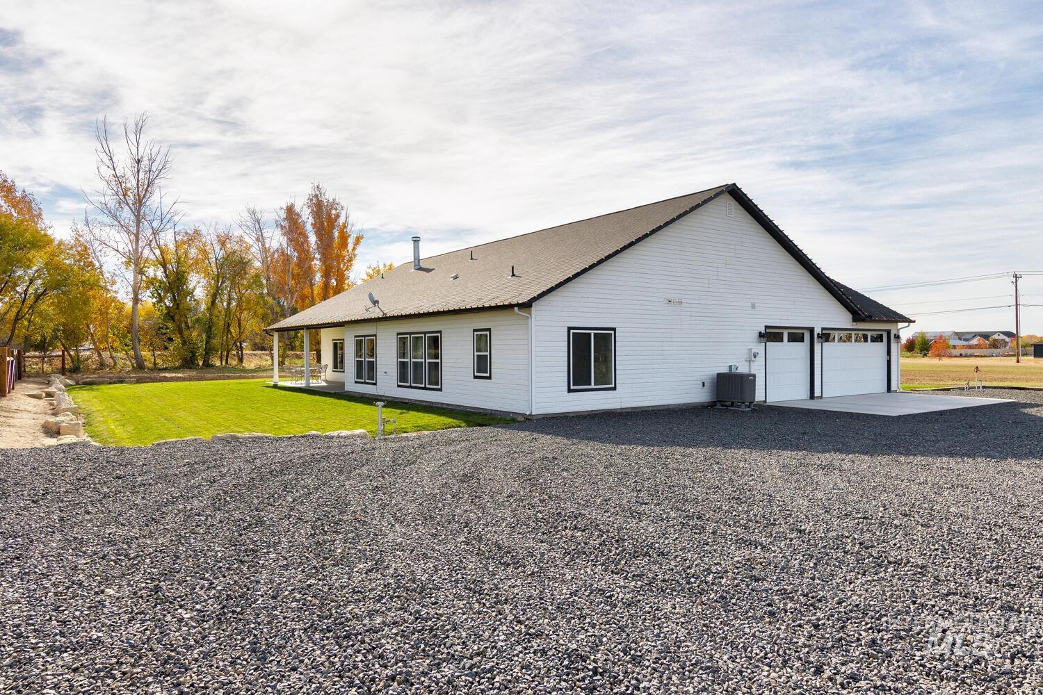 Back of house with a lawn, gravel driveway, an attached garage, and a patio