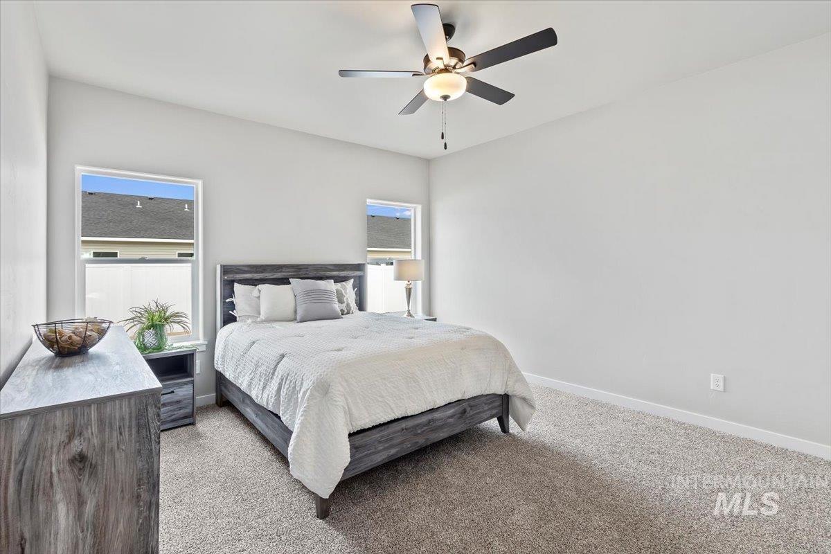 Bedroom with light carpet, multiple windows, and ceiling fan