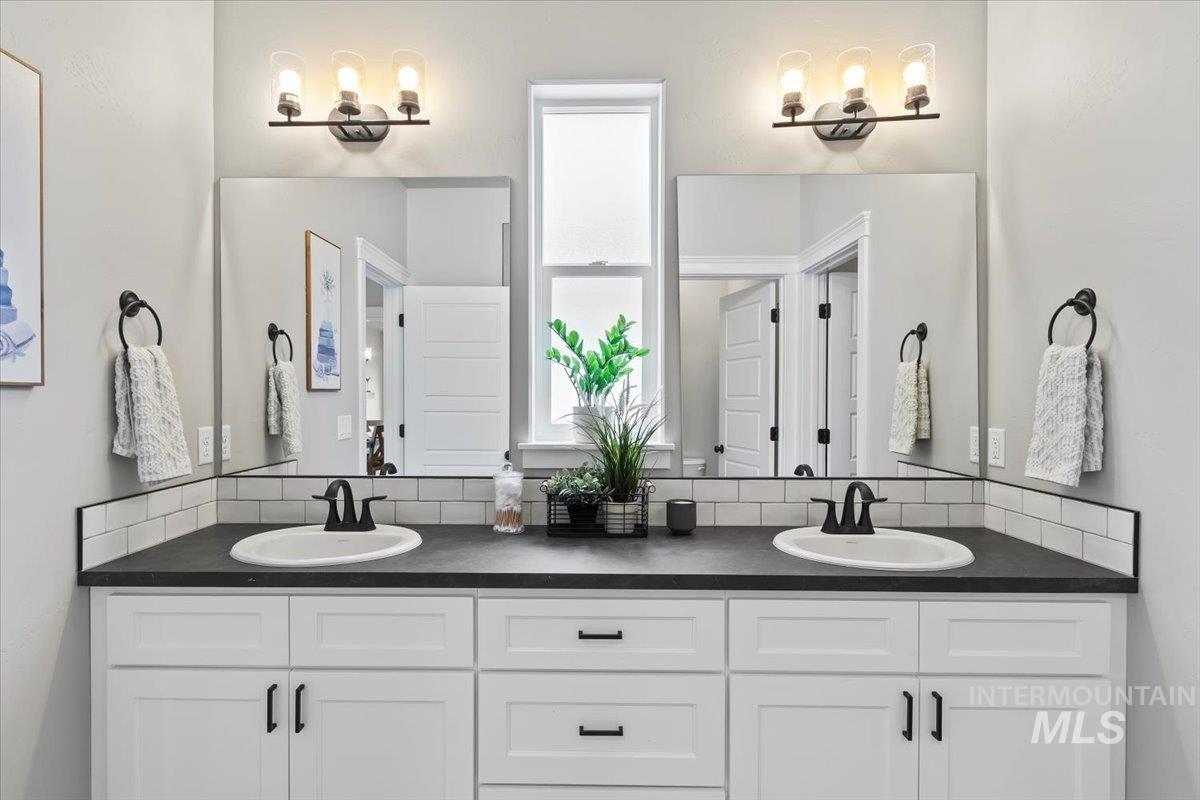 Full bathroom featuring double vanity, decorative backsplash, and a chandelier