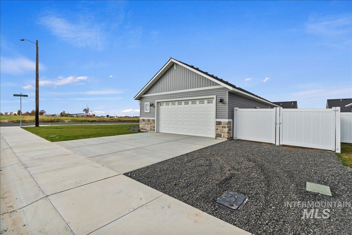 View of property exterior with stone siding, concrete driveway, a gate, a water view, and a yard