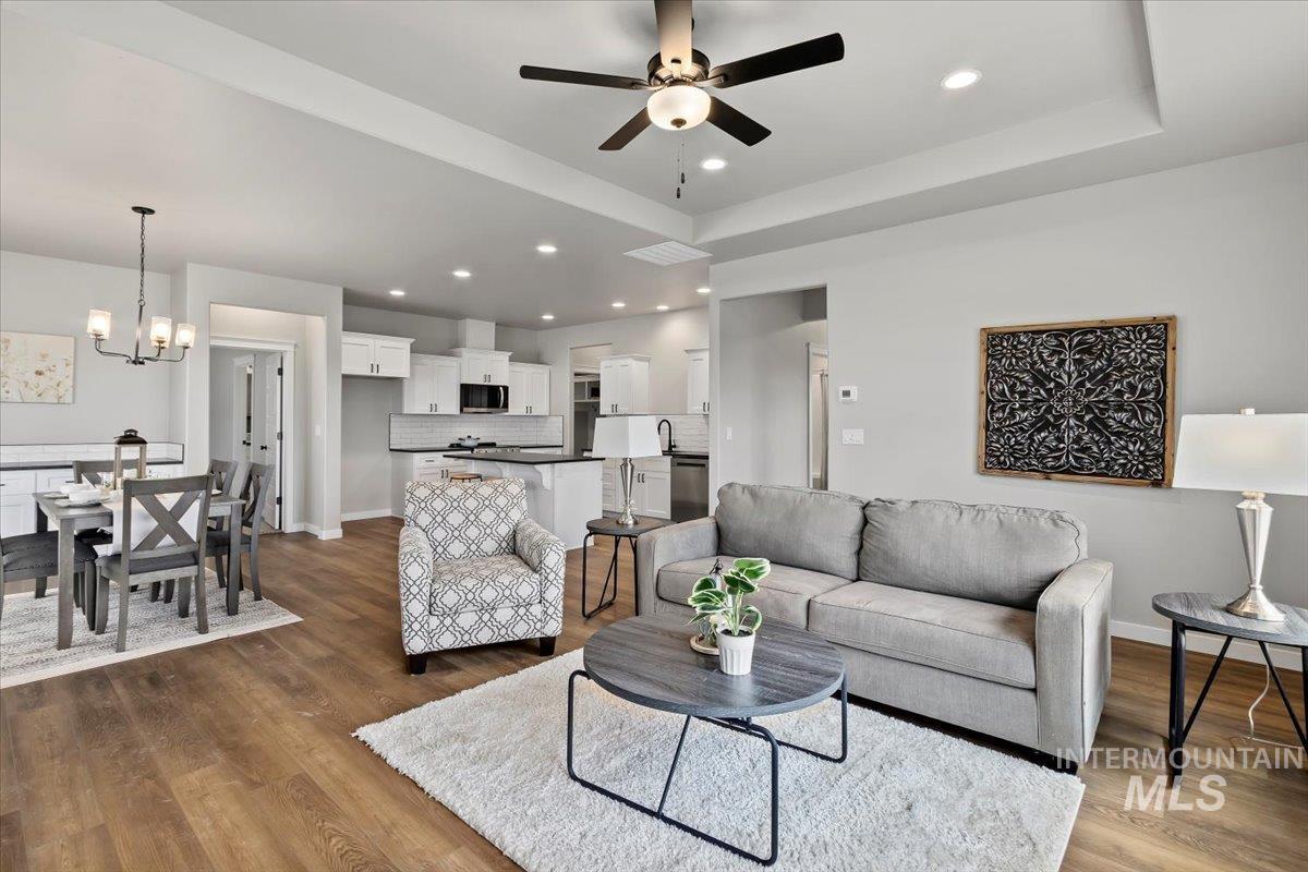 Living area with a raised ceiling, dark wood finished floors, recessed lighting, a ceiling fan, and a chandelier