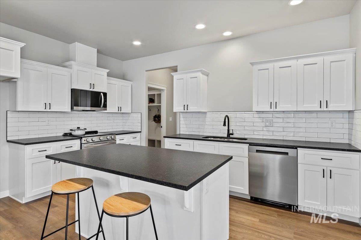 Kitchen with a kitchen breakfast bar, white cabinets, appliances with stainless steel finishes, light wood-type flooring, and dark countertops