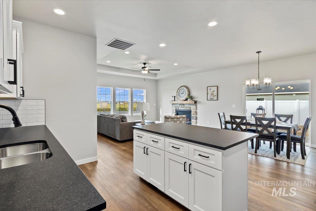 Kitchen with dark countertops, white cabinetry, hanging light fixtures, open floor plan, and light wood-type flooring