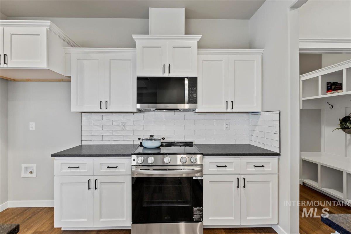 Kitchen featuring appliances with stainless steel finishes, white cabinetry, dark wood-style flooring, dark stone counters, and backsplash