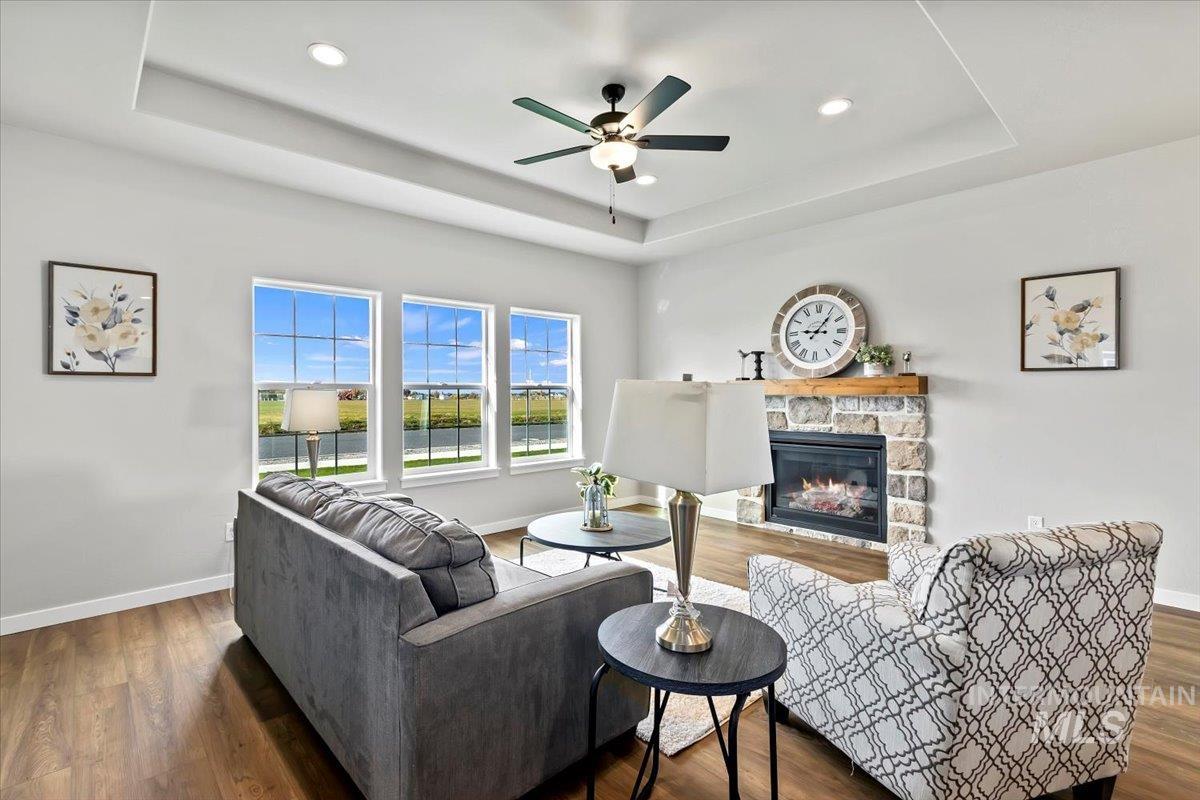 Living area featuring a raised ceiling, a fireplace, wood finished floors, a ceiling fan, and recessed lighting