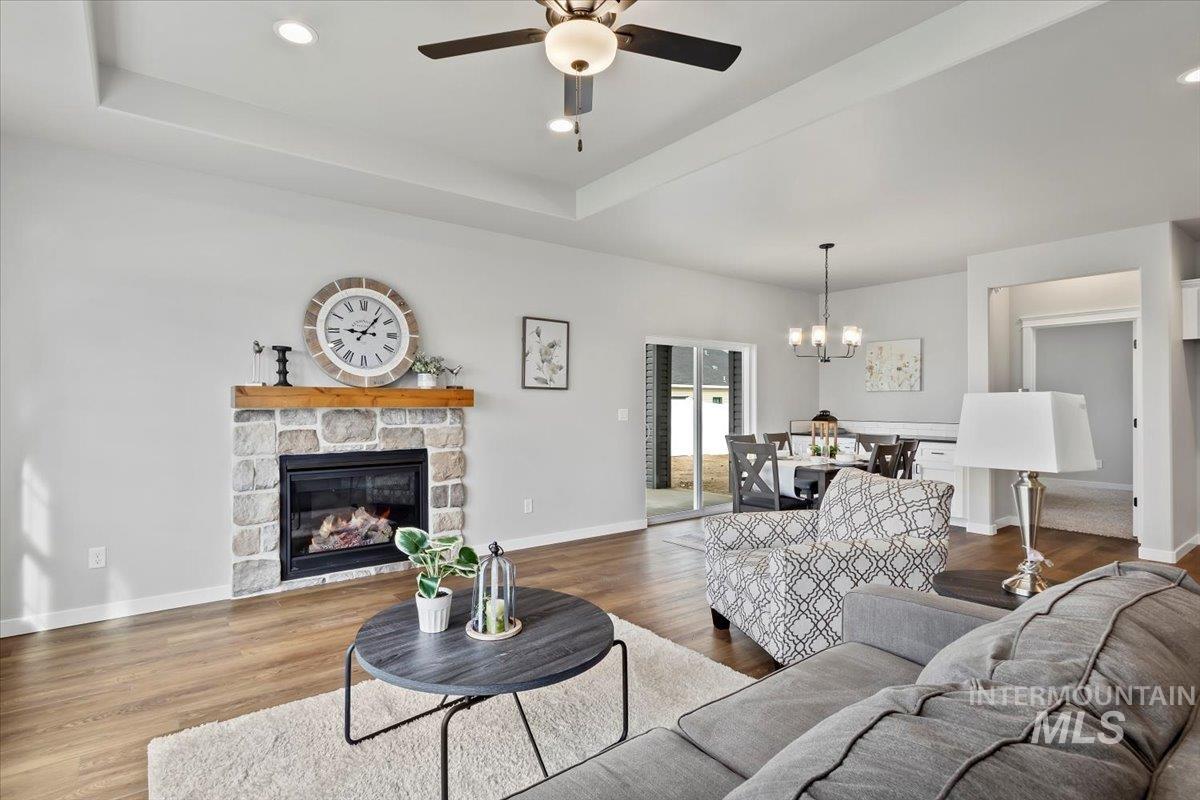 Living area featuring a raised ceiling, a stone fireplace, a chandelier, wood finished floors, and recessed lighting