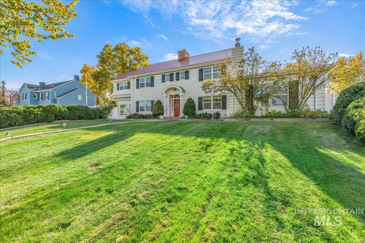 Colonial inspired home with a metal roof, a chimney, and a front yard