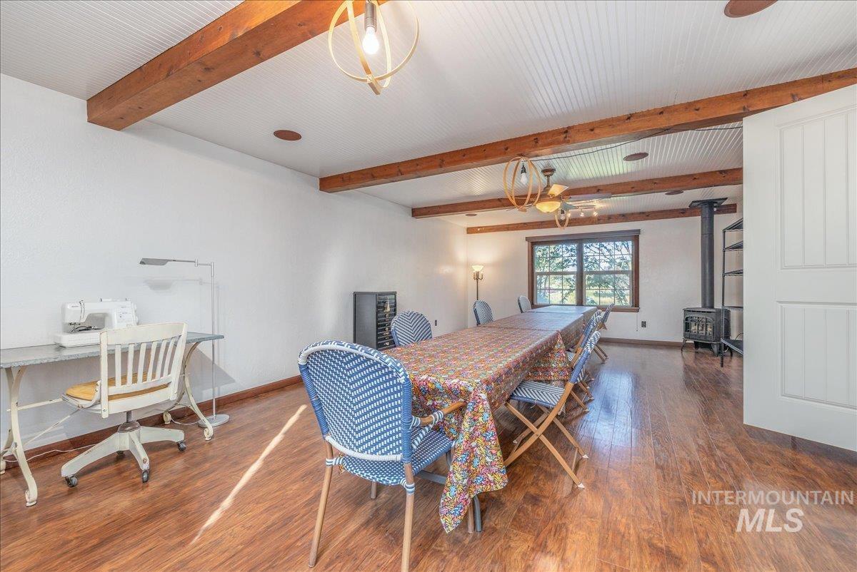 Dining area with a wood stove, wood finished floors, and beamed ceiling