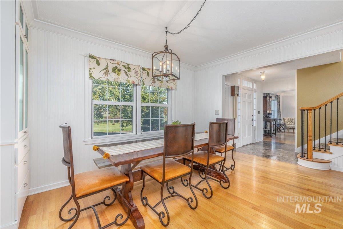 Dining room with stairs, light wood-type flooring, crown molding, and a chandelier