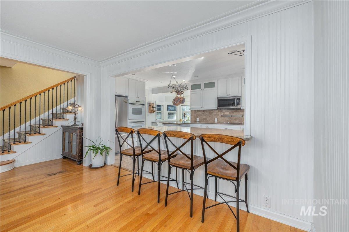 Kitchen with a kitchen bar, white cabinetry, light wood-style flooring, ornamental molding, and glass insert cabinets