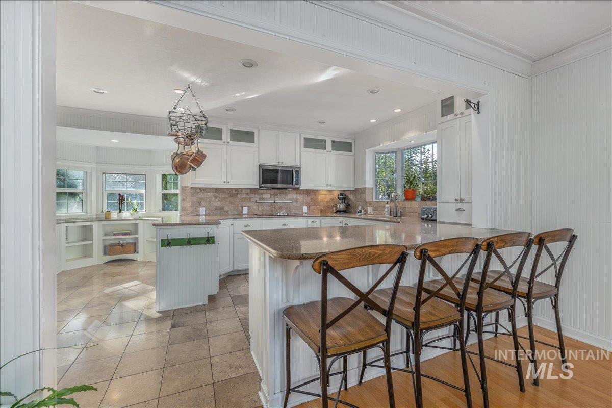 Kitchen with glass insert cabinets, a kitchen bar, white cabinets, backsplash, and crown molding