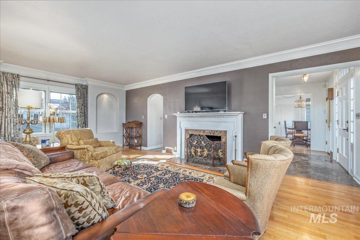 Living area with ornamental molding, wood finished floors, a high end fireplace, and arched walkways