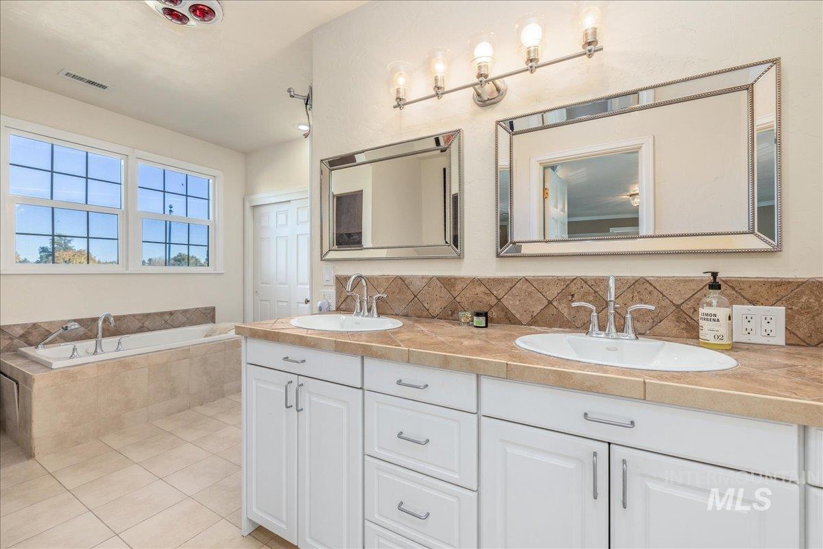 Full bath featuring double vanity, a garden tub, light tile patterned floors, and tasteful backsplash