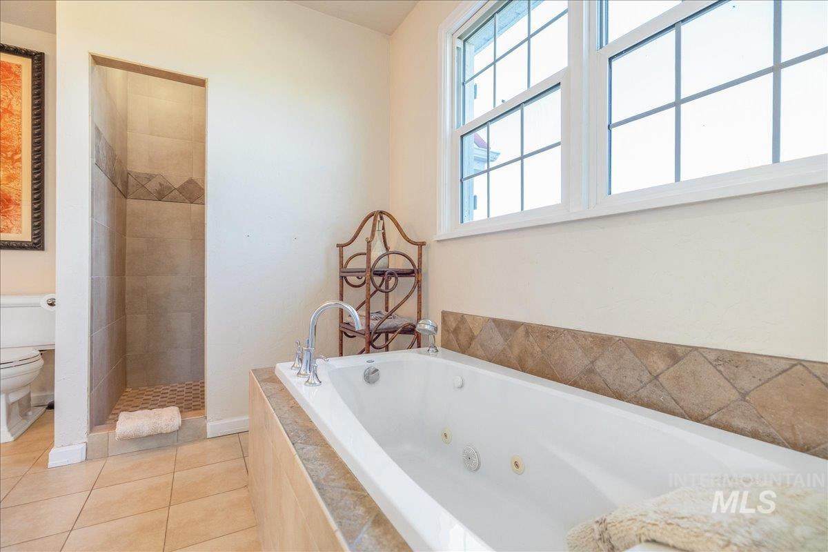 Bathroom with a tub with jets, walk in shower, and light tile patterned flooring