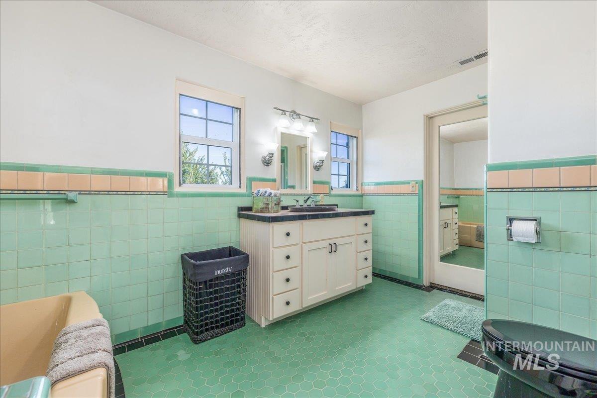 Full bathroom featuring wainscoting, tile walls, vanity, dark tile patterned floors, and a textured ceiling
