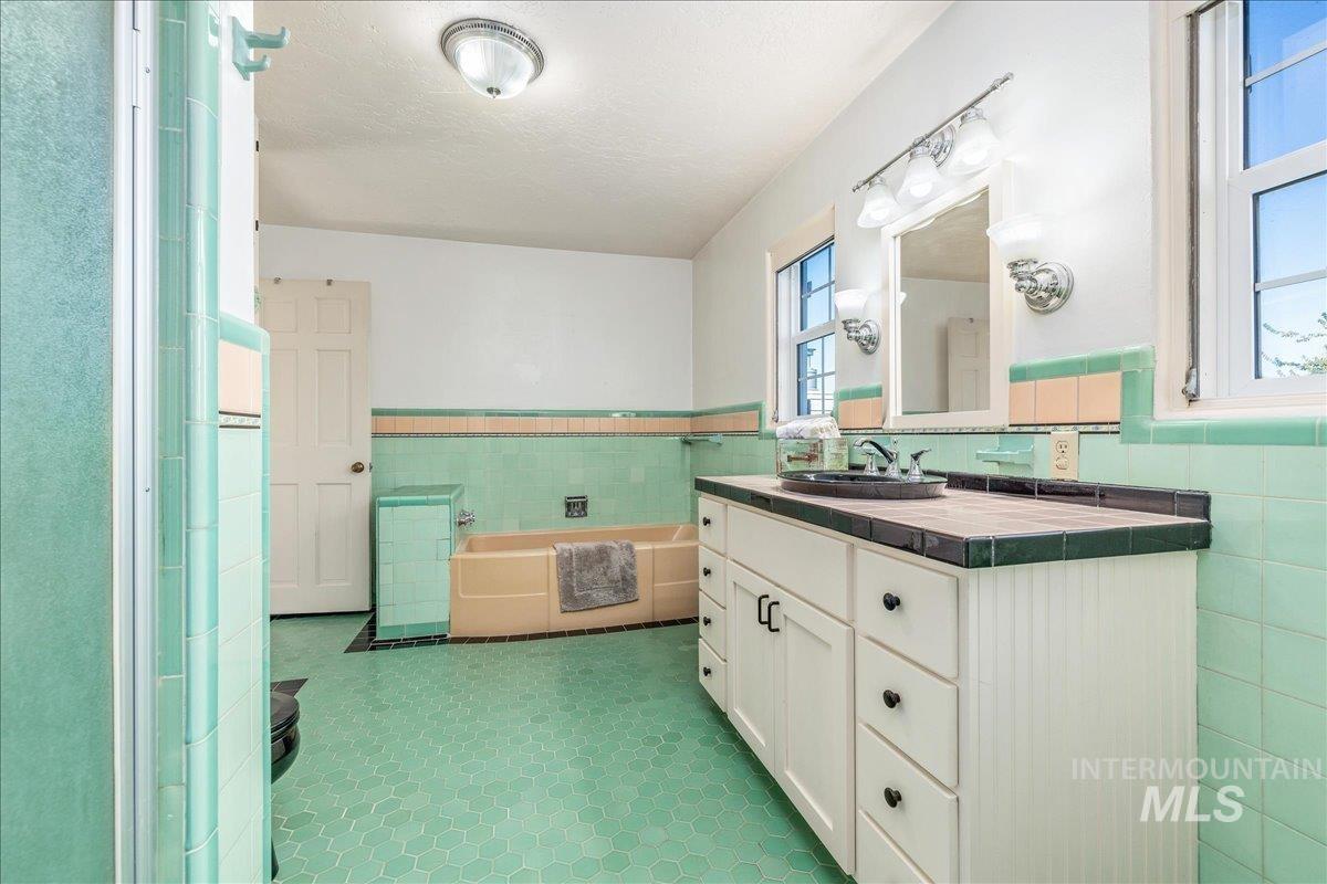 Full bath with tile walls, wainscoting, a bath, vanity, and a textured ceiling