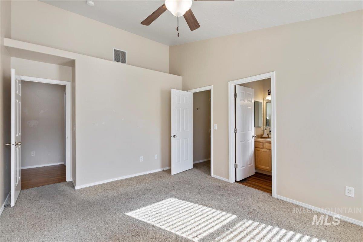 Unfurnished bedroom featuring carpet, ensuite bathroom, and ceiling fan