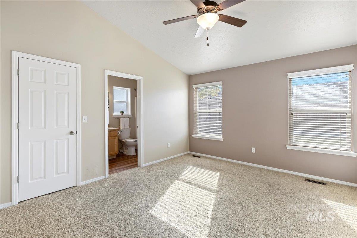 Unfurnished bedroom with lofted ceiling, ensuite bathroom, carpet, and ceiling fan
