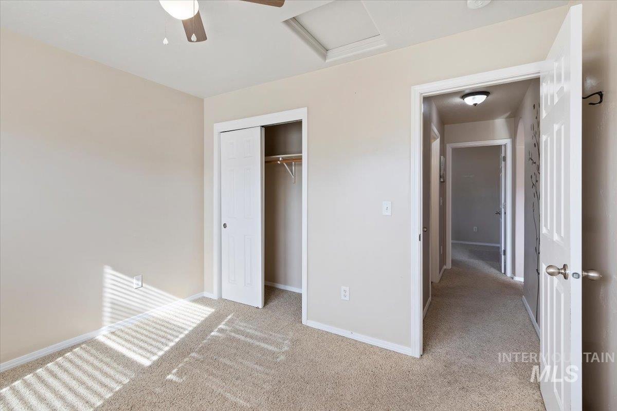 Unfurnished bedroom with attic access, light colored carpet, a closet, and a ceiling fan