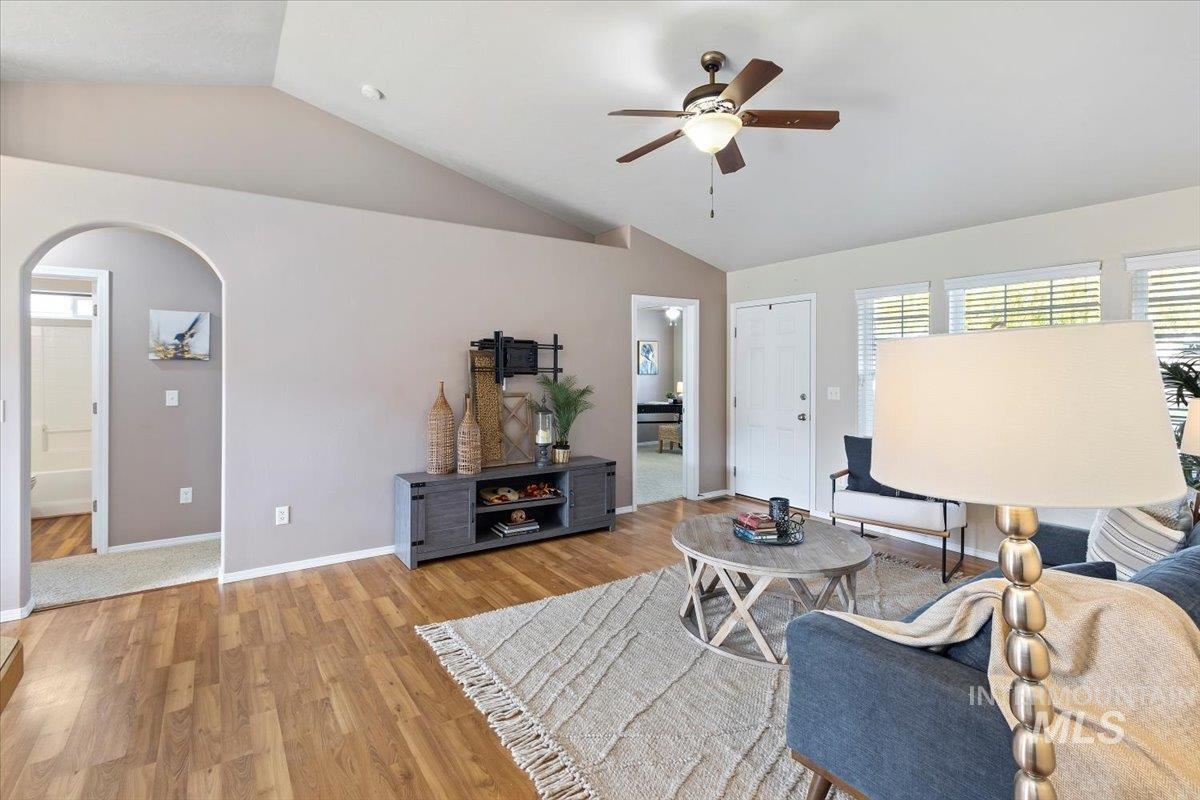 Living room featuring wood finished floors, vaulted ceiling, arched walkways, and ceiling fan