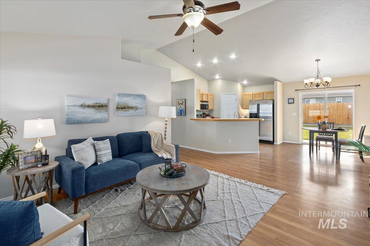 Living area featuring light wood finished floors, a chandelier, a ceiling fan, and high vaulted ceiling