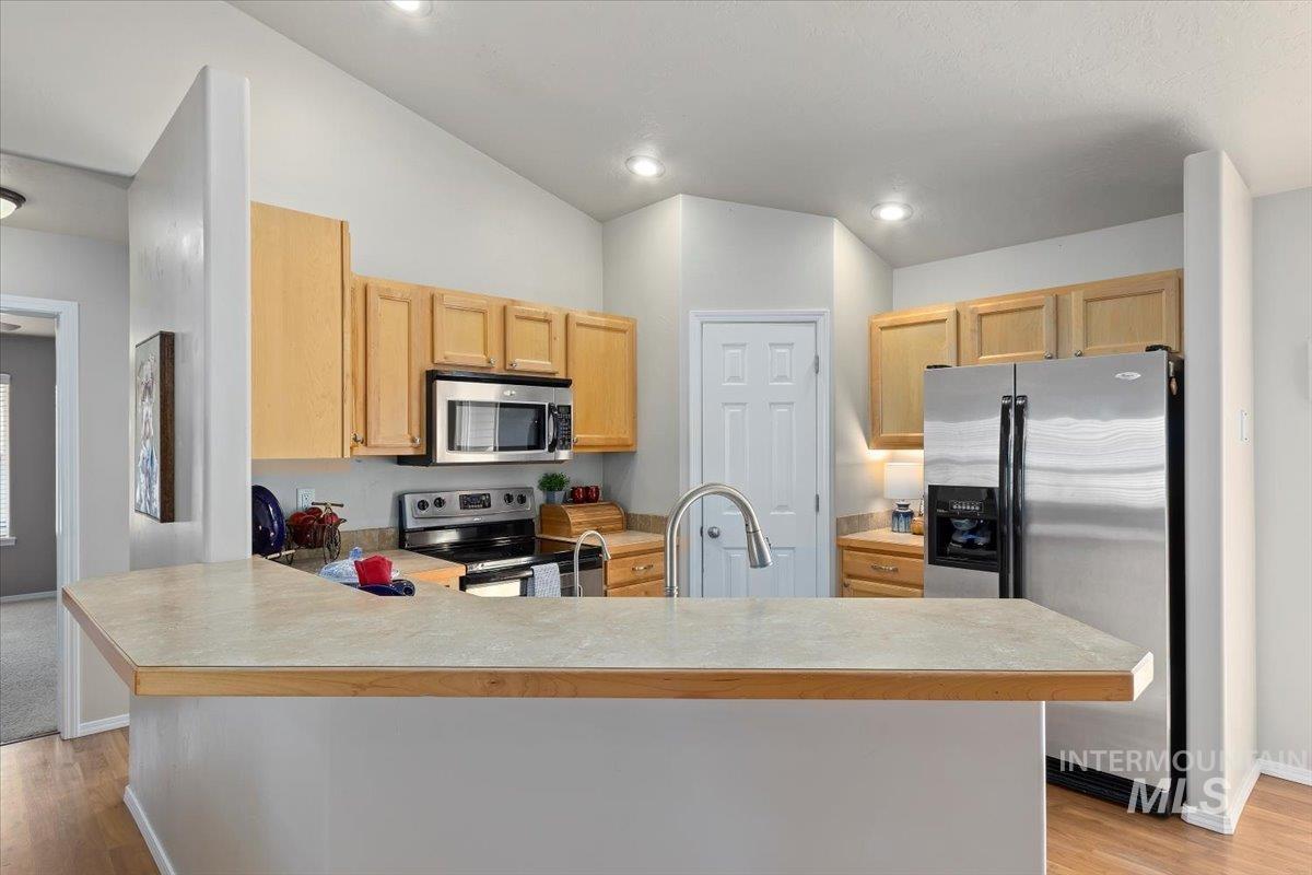 Kitchen featuring light countertops, stainless steel appliances, light wood-style floors, light brown cabinetry, and vaulted ceiling